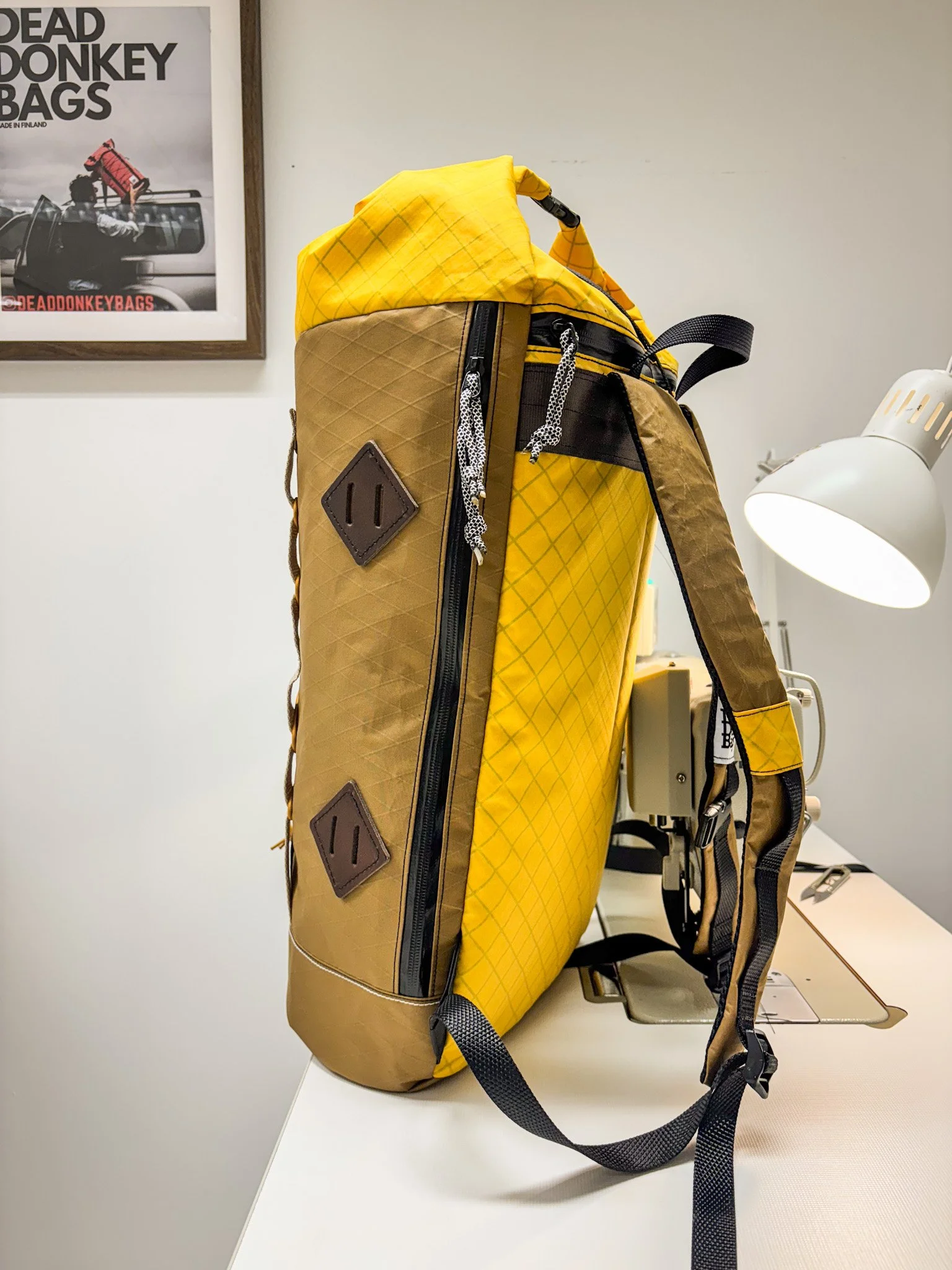 A yellow and brown outdoor backpack placed on a desk near a white desk lamp.