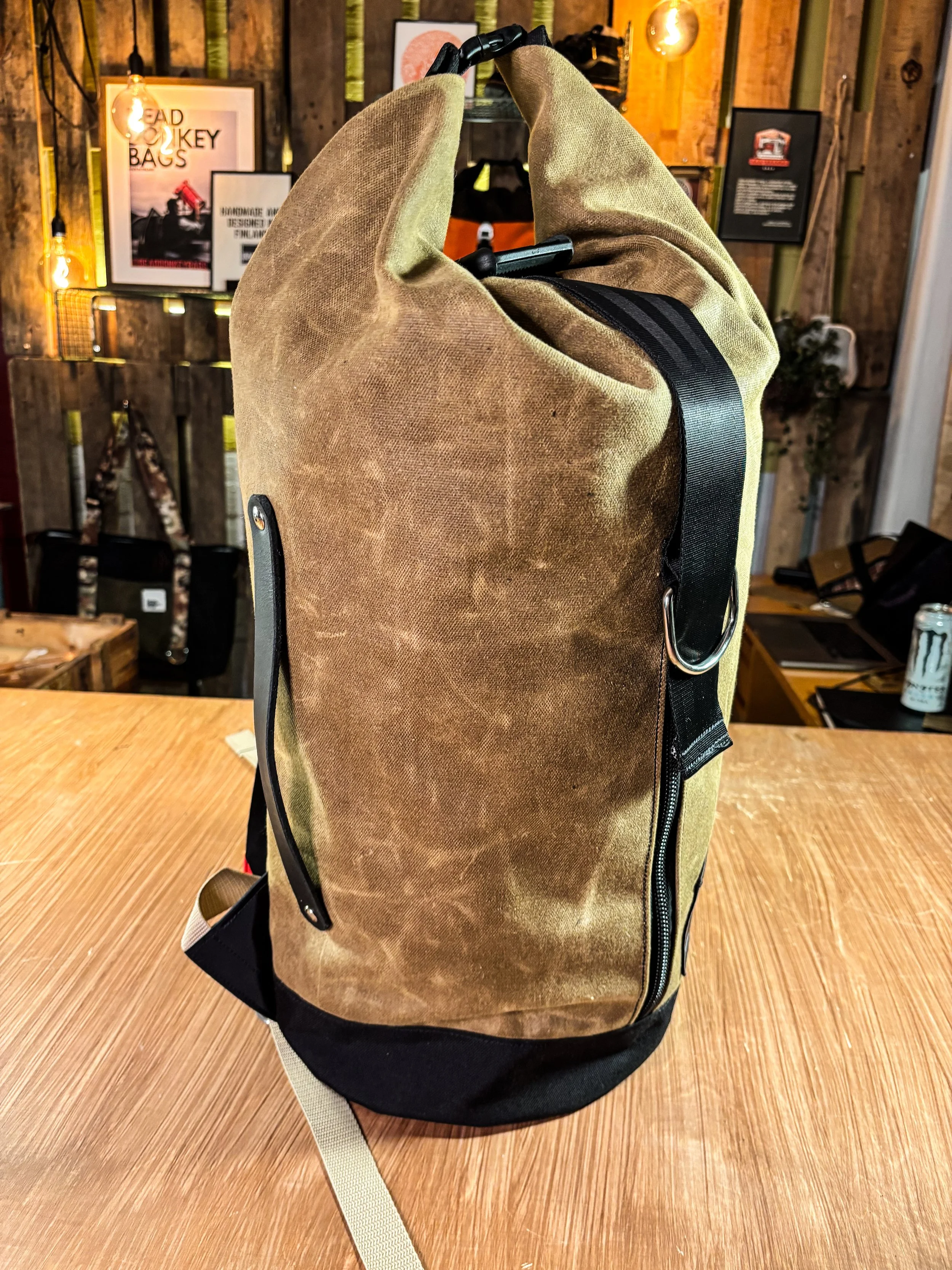 A tan canvas backpack with black accents, placed upright on a wooden table in a rustic setting.