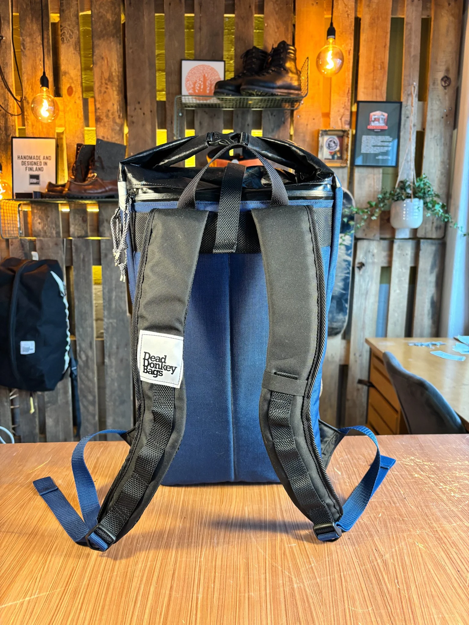 Backpack with padded shoulder straps on a wooden table in a retail store with wooden wall decor and footwear display.