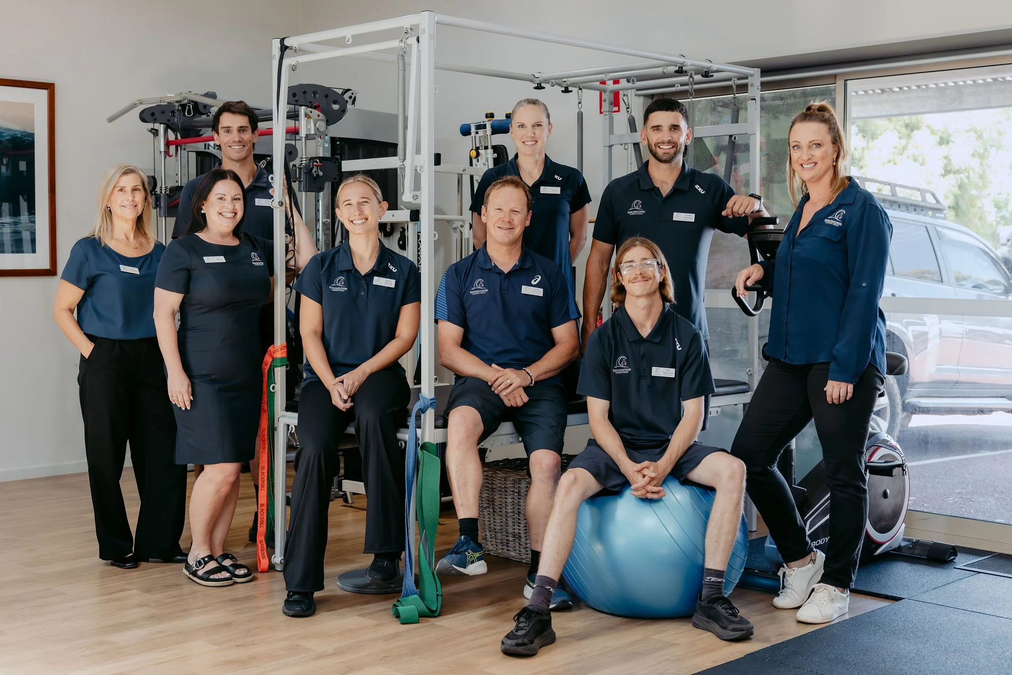 Team of physical therapists and trainers posing in a rehab or training center with exercise equipment and therapy tools.