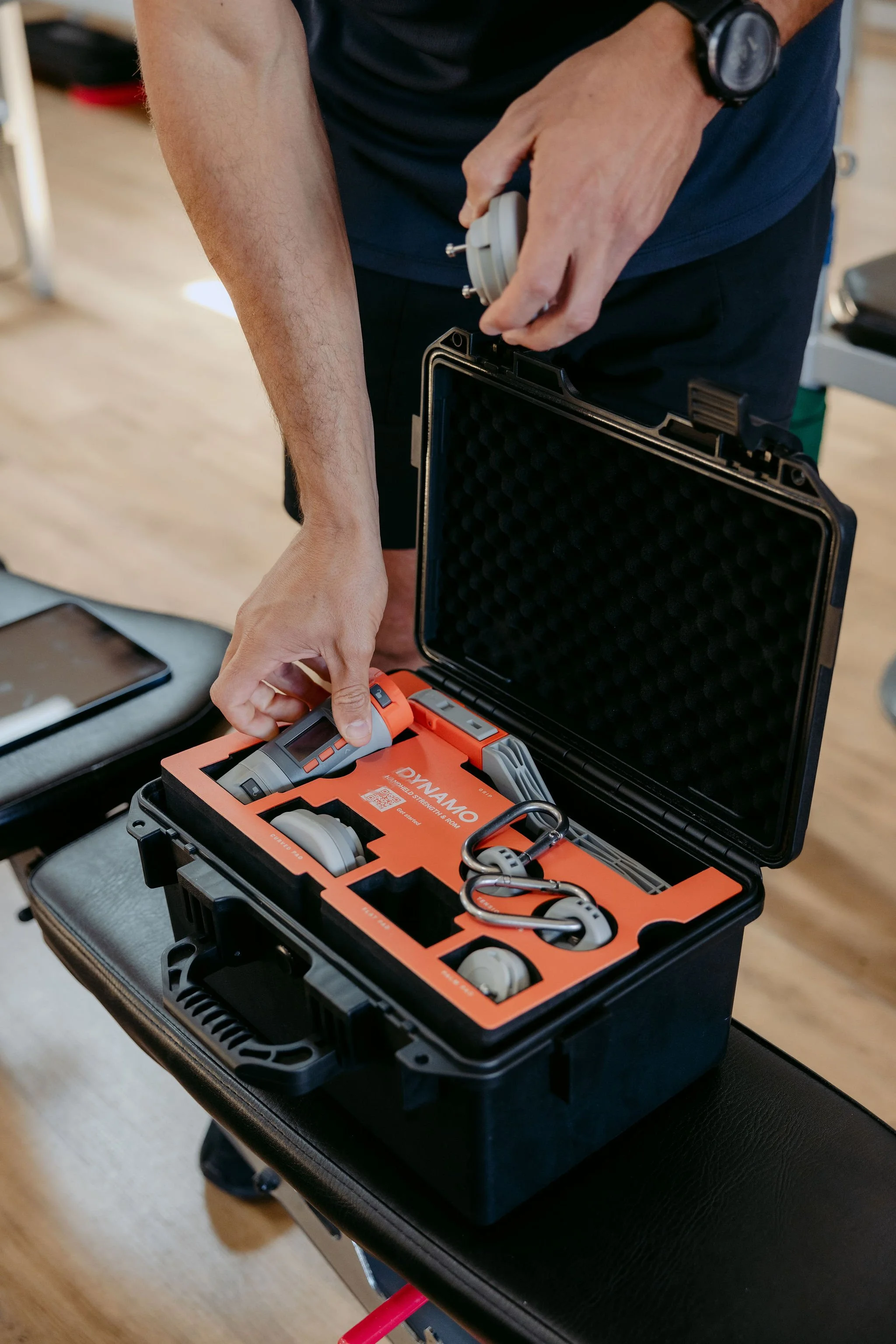A person is assembling or inspecting a wearable EMS device inside a black carrying case, set on a table.