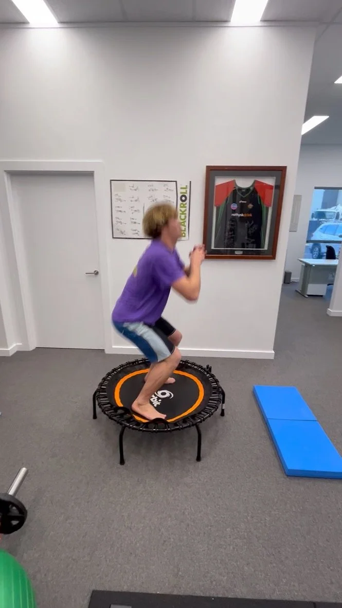 A young boy jumping on a small trampoline indoors at a gym or recreational facility.