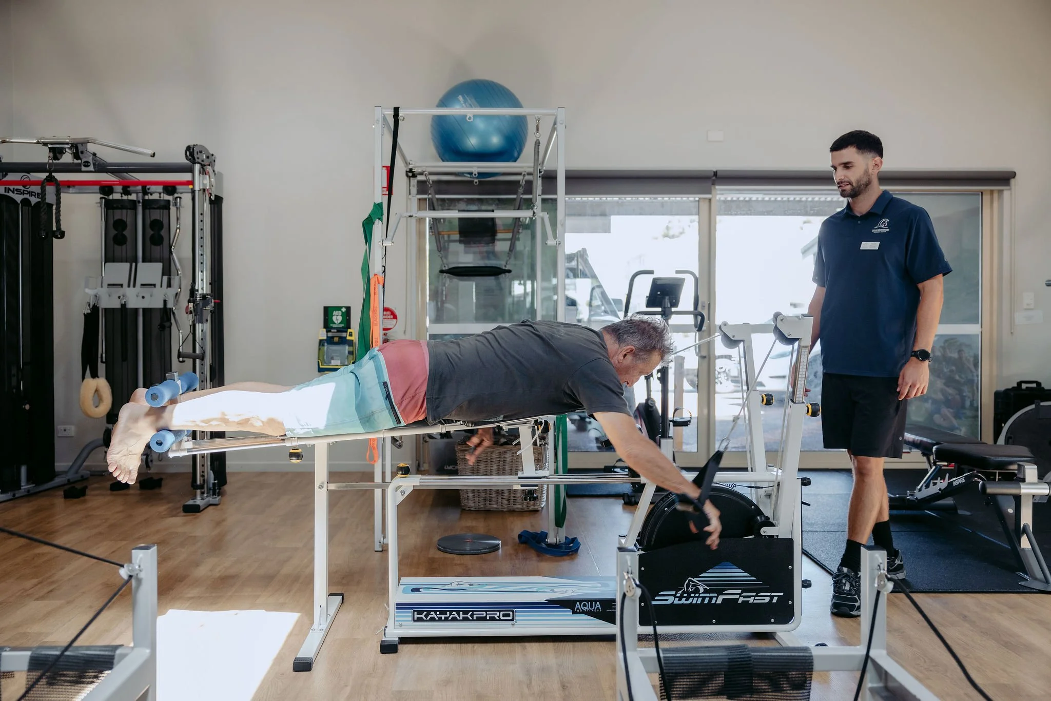 A man doing physical therapy exercises on a specialized treadmill in a rehabilitation center with a therapist monitoring.