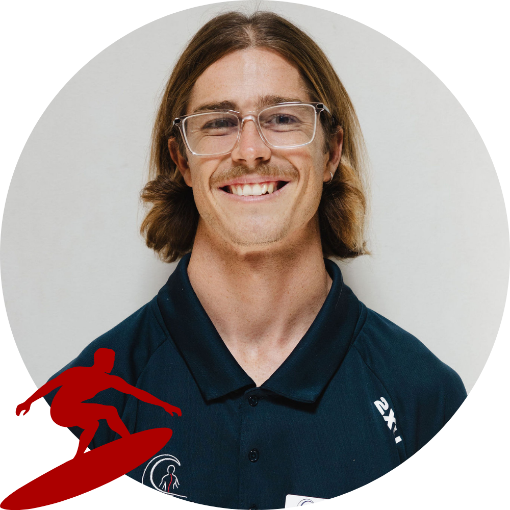 A young man with medium-length light brown hair, glasses, and a mustache, smiling and wearing a dark sports shirt with logos.