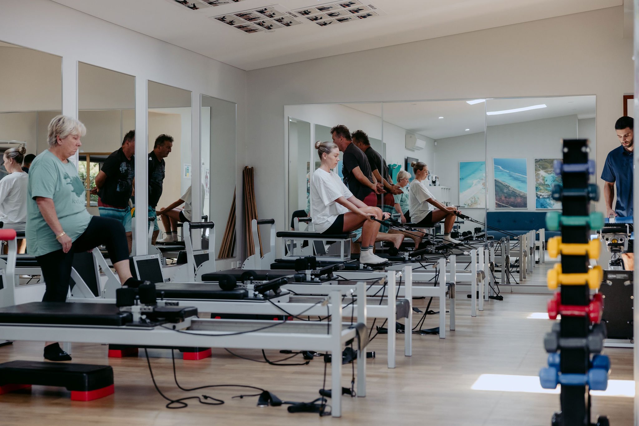 Group of people exercising on Pilates reformer machines in a fitness studio, with mirrors and art on the walls