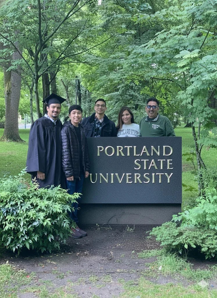 Five people standing behind a sign that reads 'Portland State University,' surrounded by green trees and bushes.