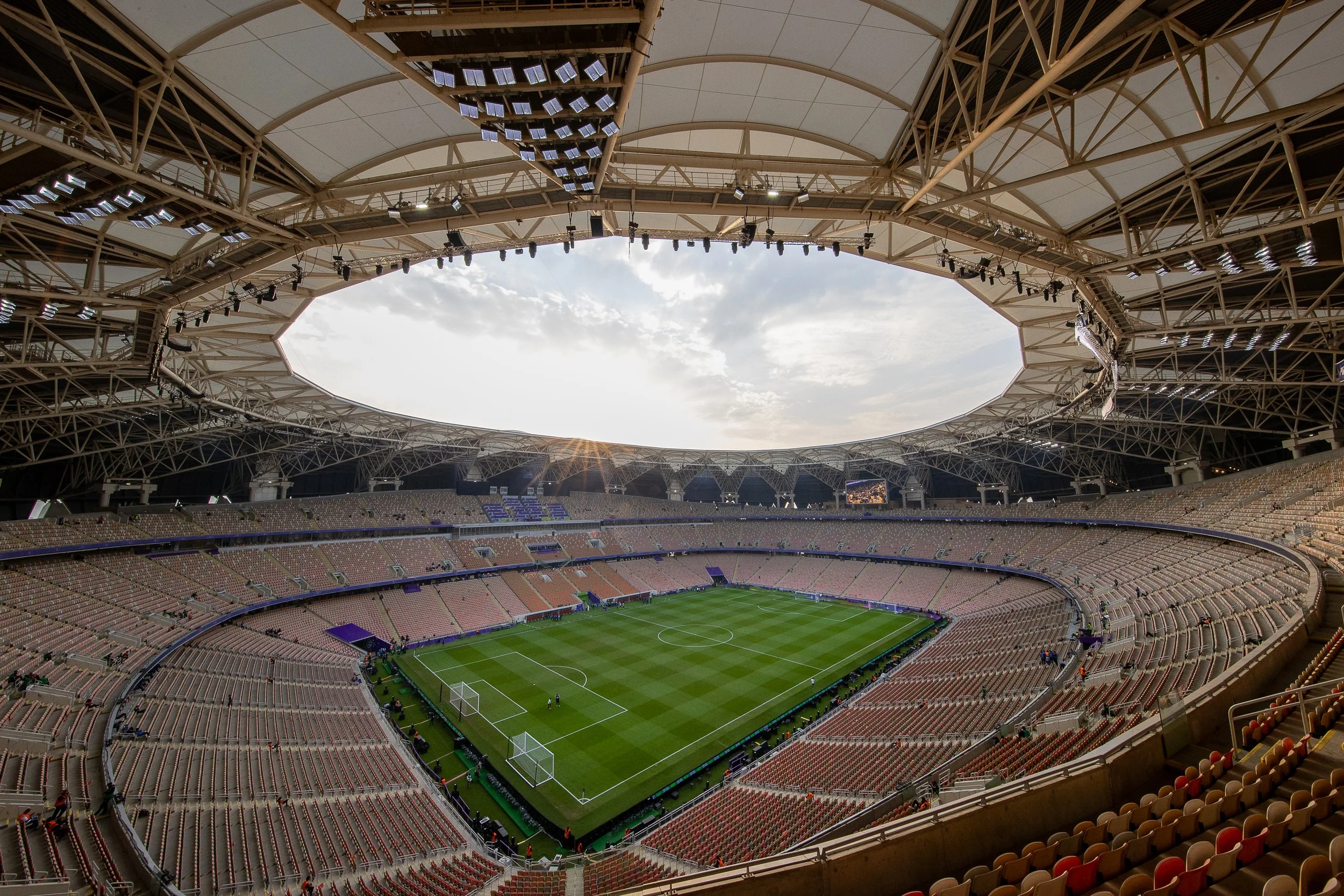Empty King Abdullah Sports City Stadium, lots of seating, and a large skylight ceiling with sunlight shining through.