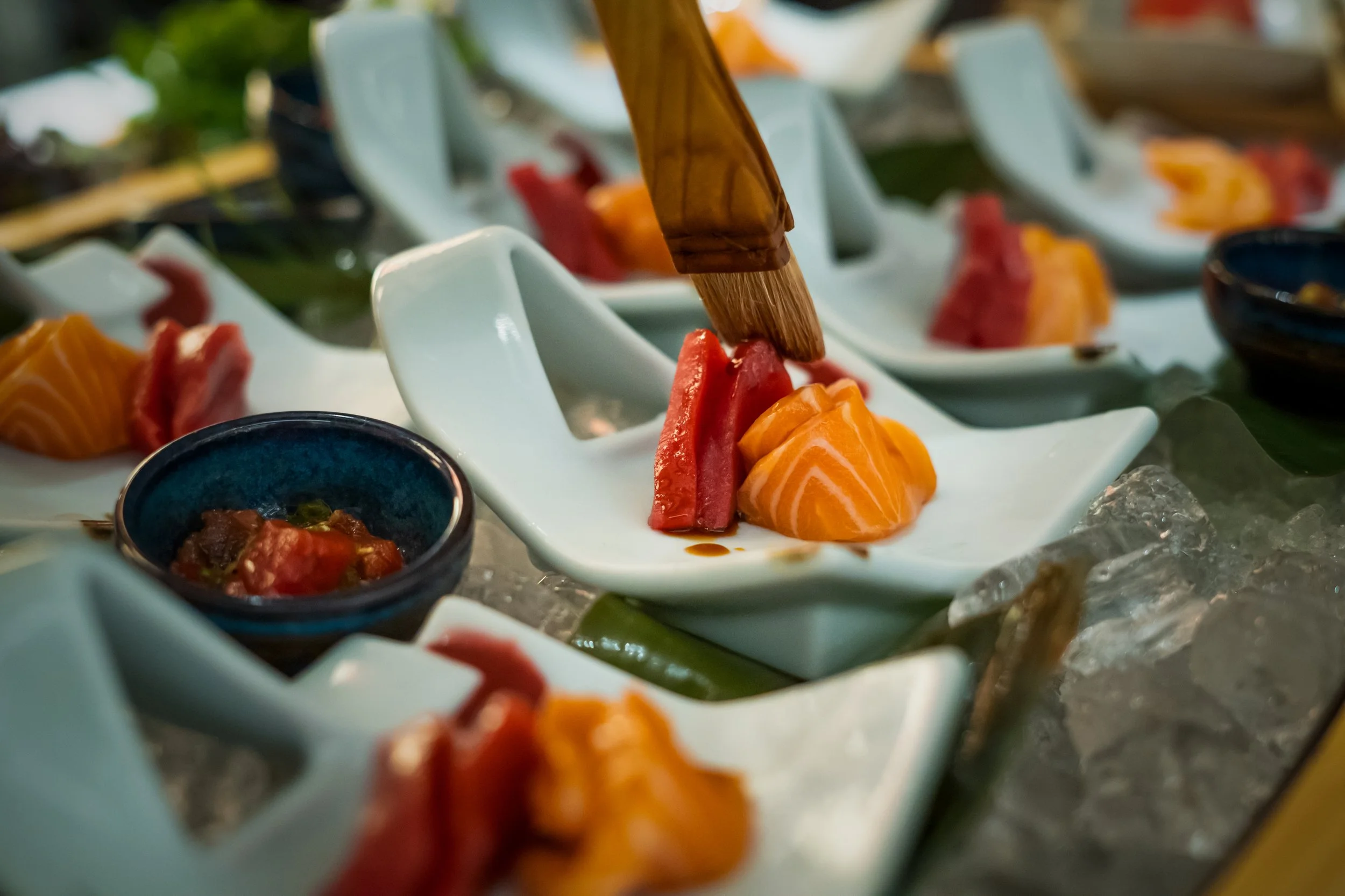 Various sashimi slices, including salmon and tuna, served on small white dishes and a small bowl, with chopsticks decorating the presentation, on a bed of ice.
