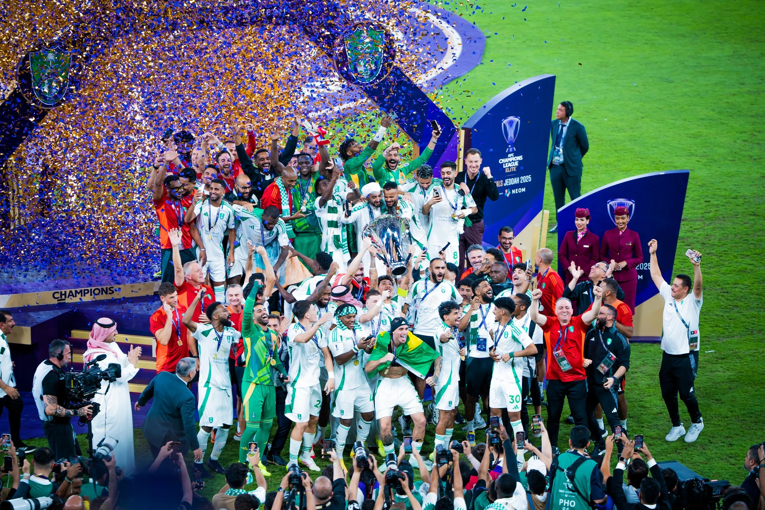 Celebrating team on stage at AFC Champions League Elite Finals Jeddah with confetti, holding trophy, surrounded by fans, with officials and camera crew.