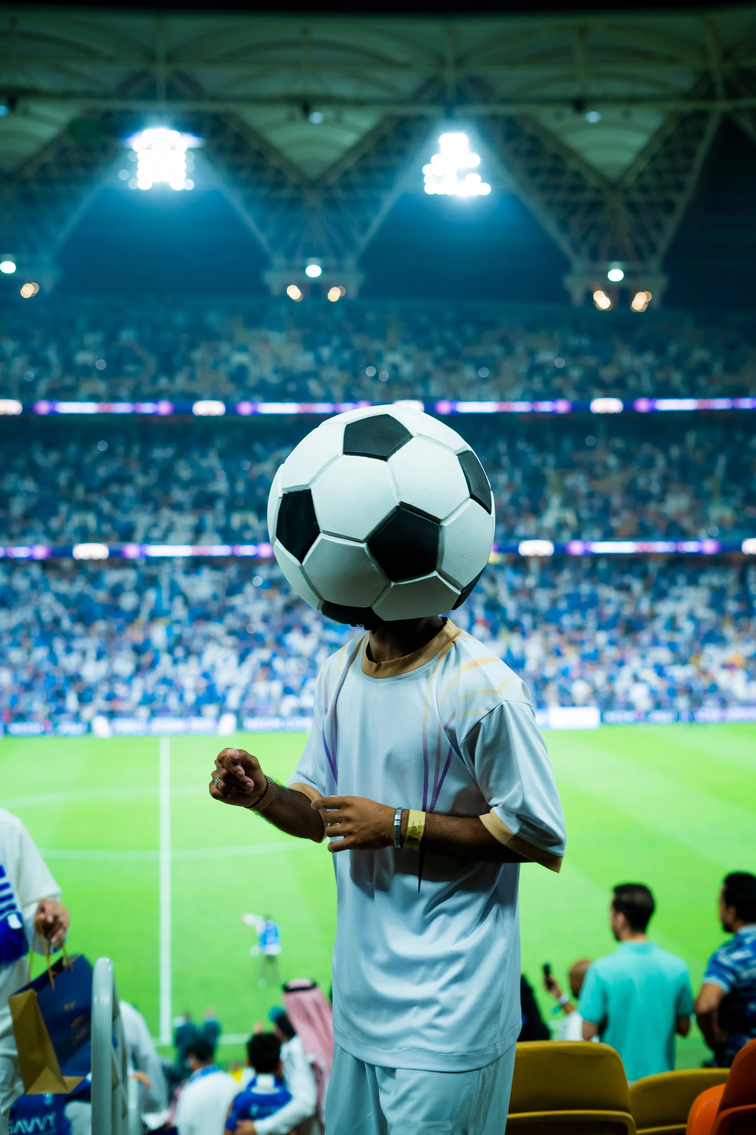 Person at the AFC Champions League Elite Finals Jeddah stadium wearing a mask shaped like a football, with a crowded stadium background.