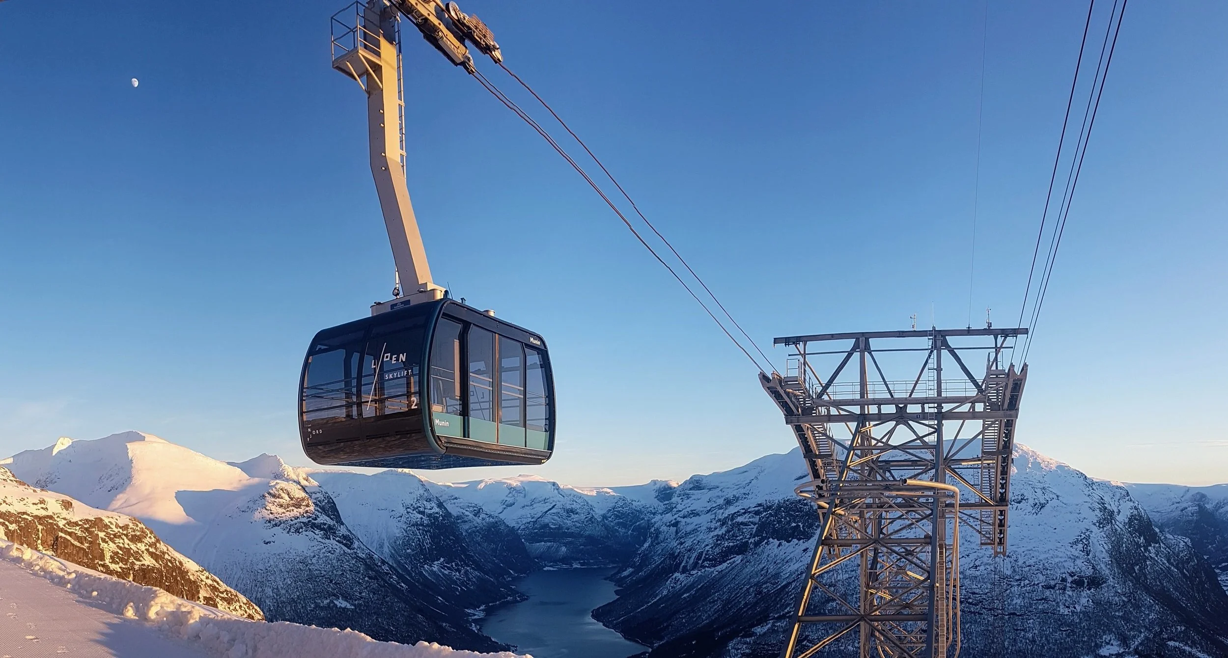 A cable car floating in the air above snow-covered mountains and fjord in a winter landscape in Loen.