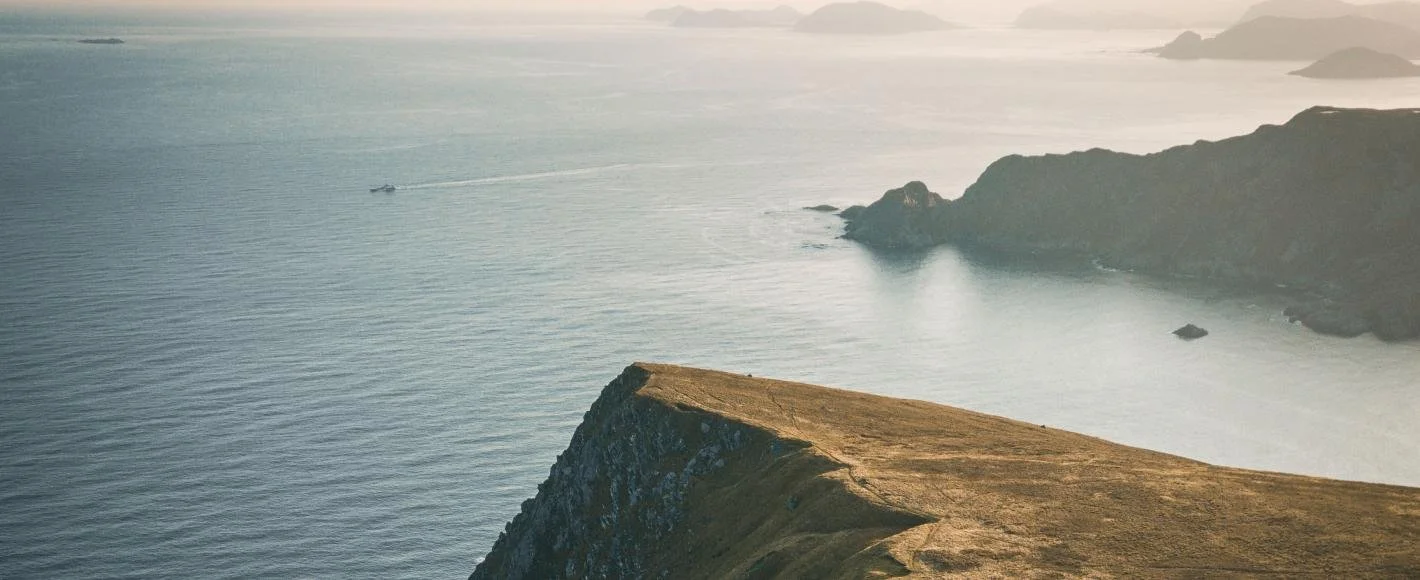 Aerial view of a cliff overlooking the ocean with a boat leaving a trail in the water