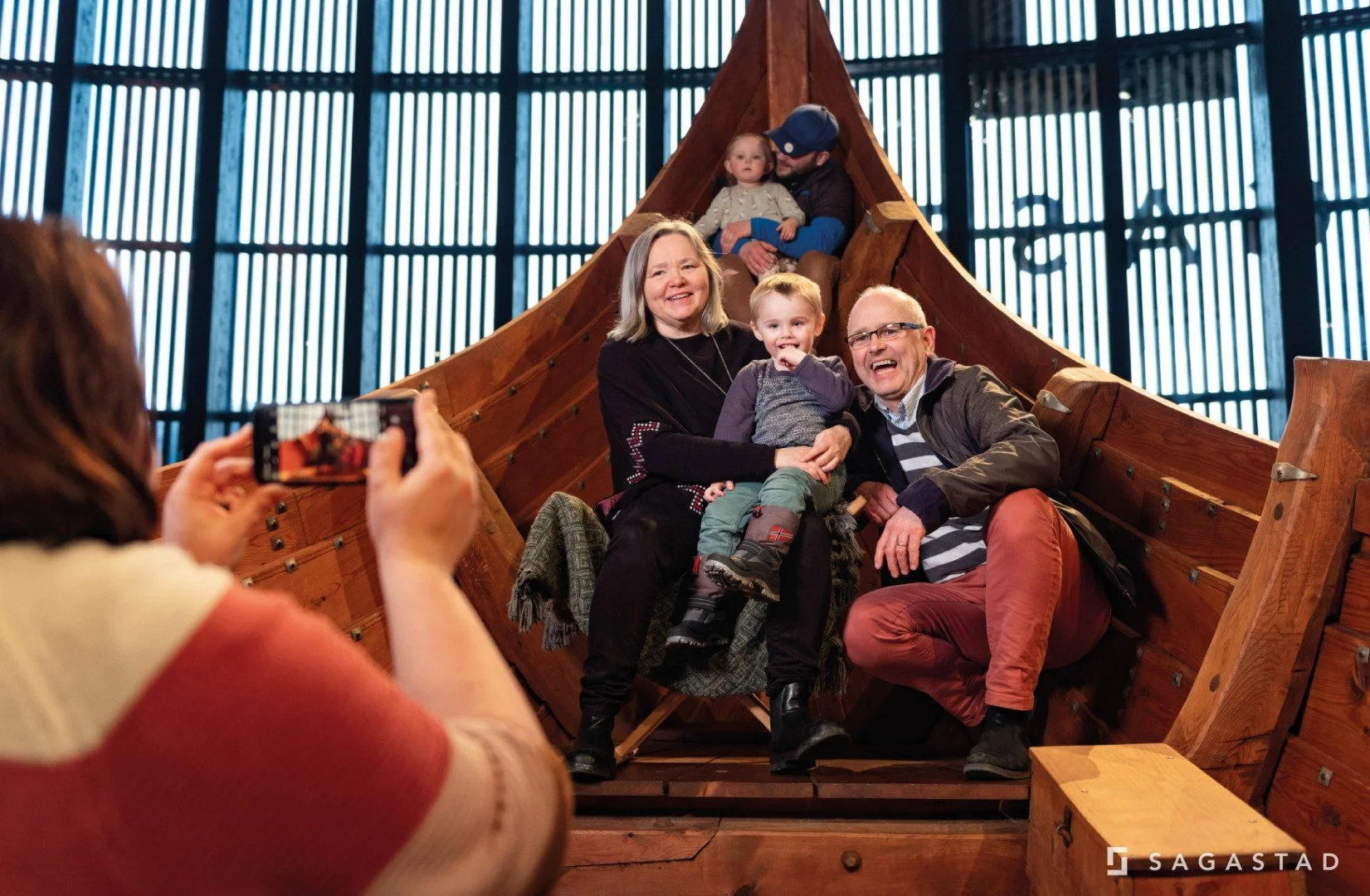 Family of four taking a selfie inside a wooden Viking ship replica, with two children and two adults smiling.