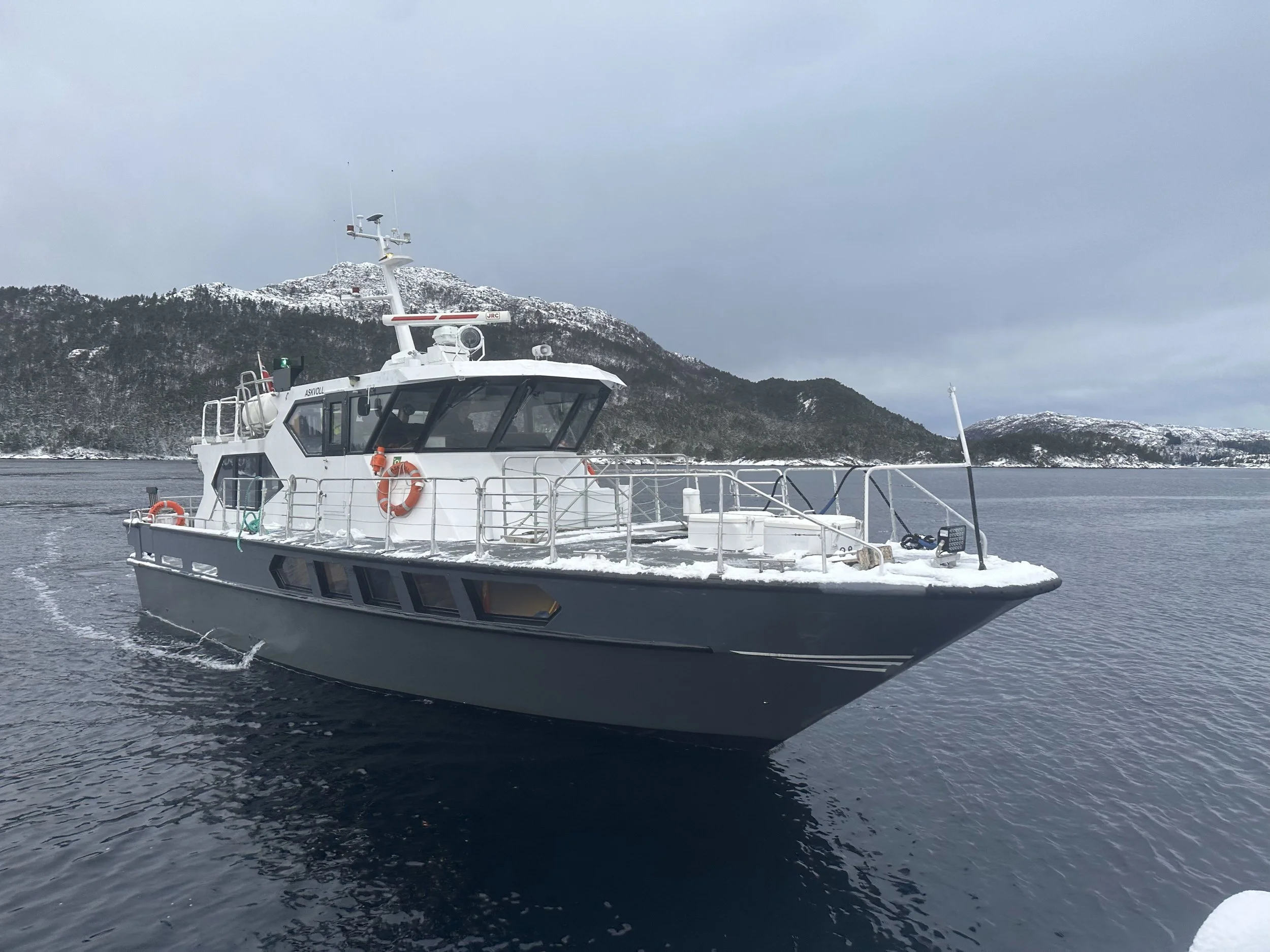 A white boat sailing in water with a snowy mountain in the background under a cloudy sky.