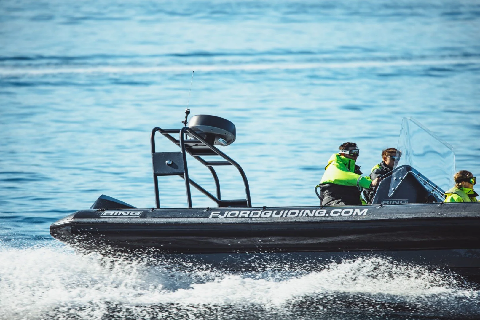 A speedboat on the water with three people wearing life jackets and sunglasses onboard.