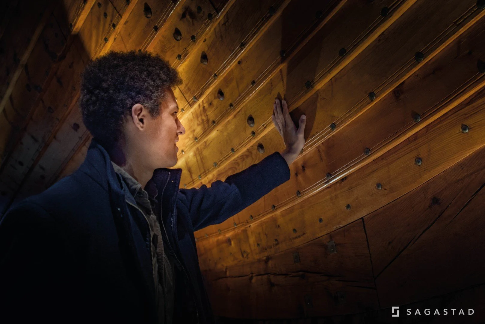 A man touching a wooden wall or ceiling in a dimly lit room.