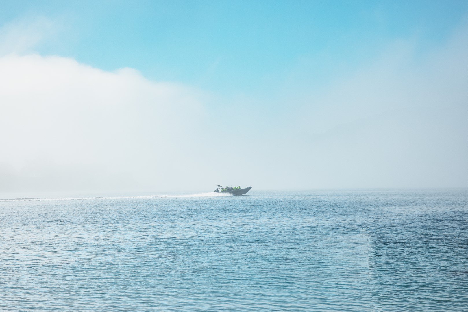 A boat speeding across a calm ocean, leaving a wake behind it on a mostly clear day with some clouds in the sky.