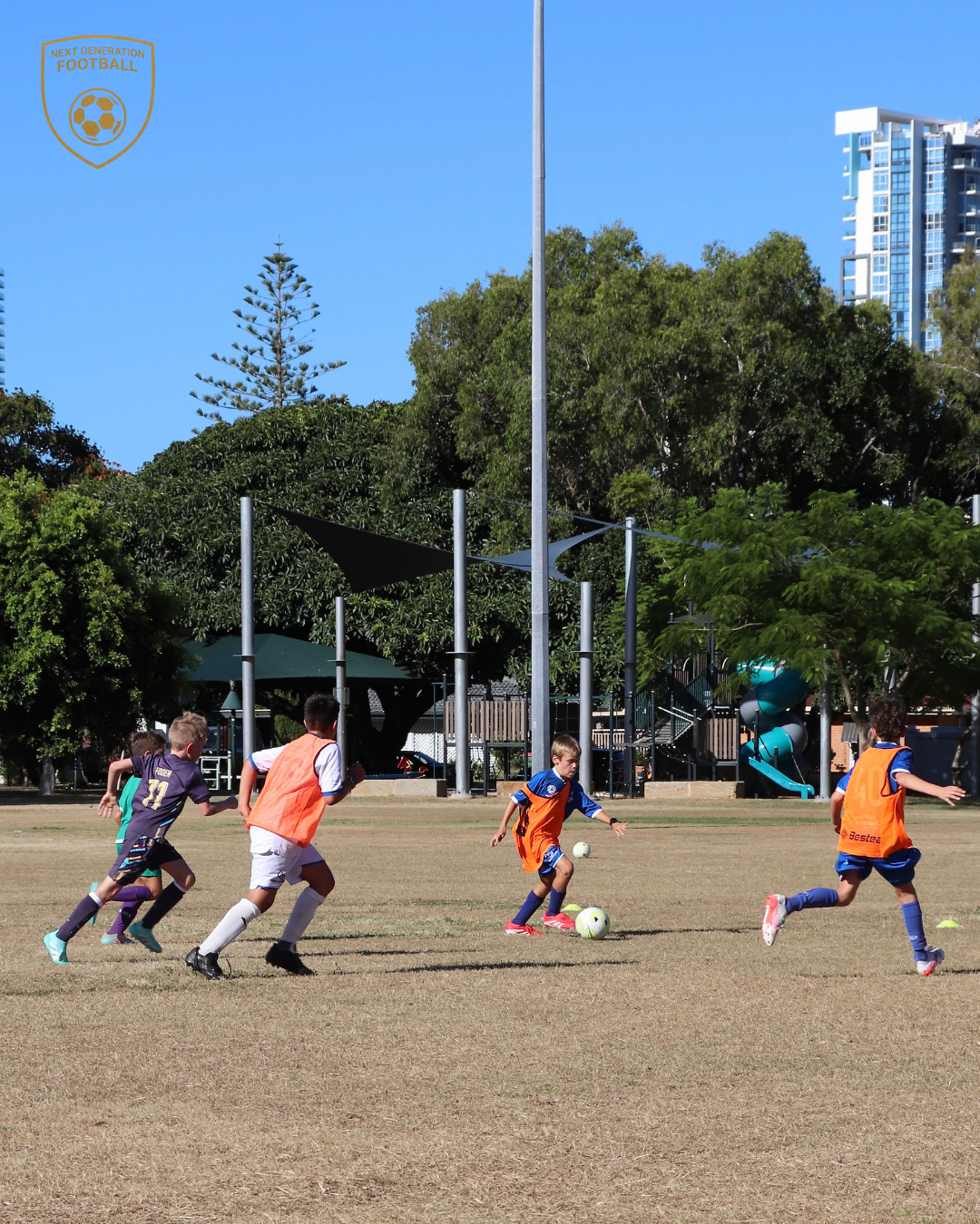 Young boys playing soccer on a field with trees and high-rise buildings in the background.