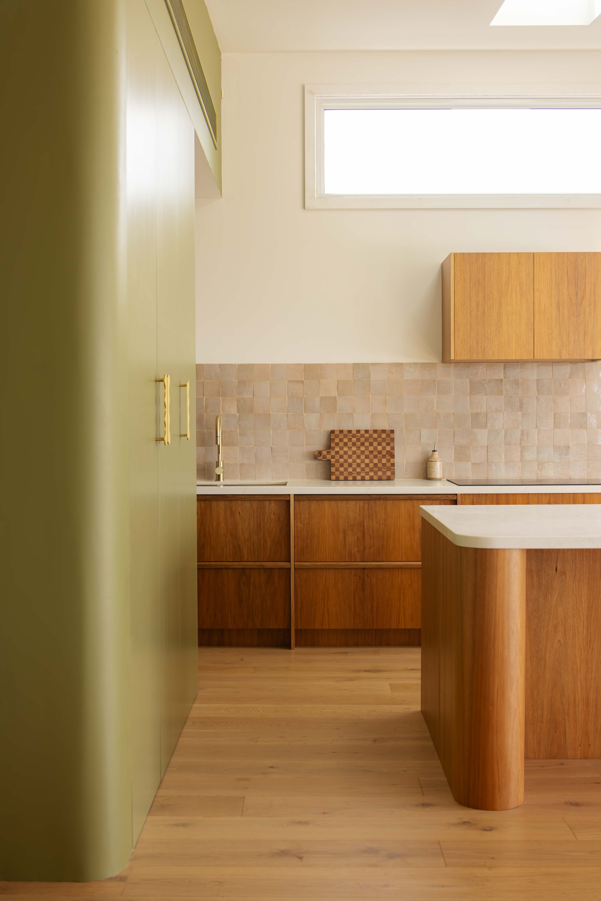 Kitchen with wooden cabinets, a green tall cabinet, a window, and a beige tiled backsplash.