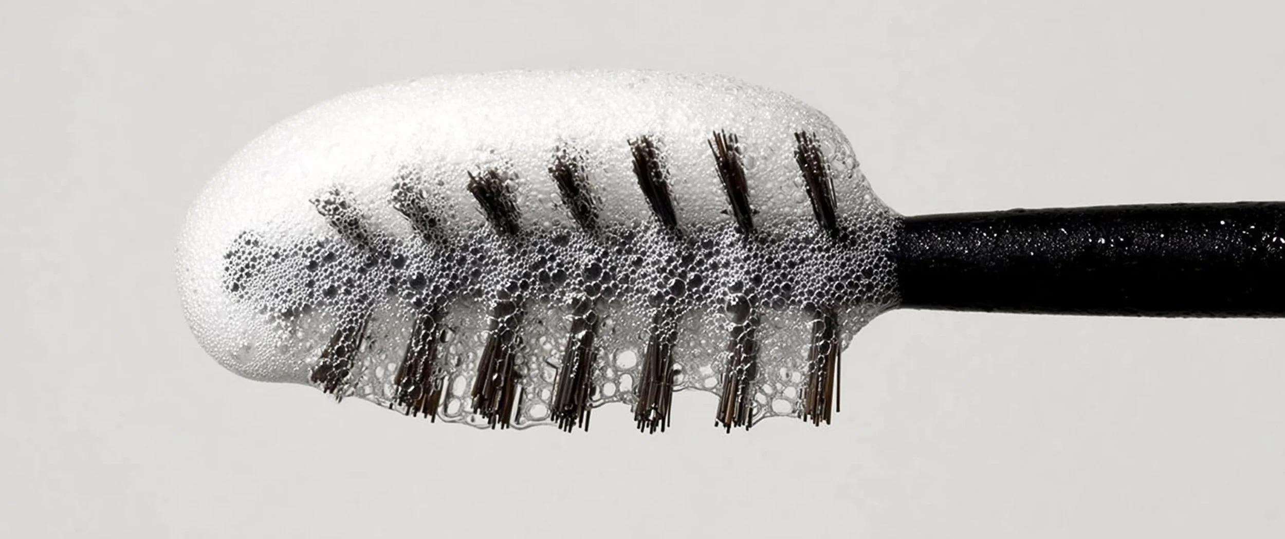 Close-up of a black toothbrush with soap bubbles on the bristles.