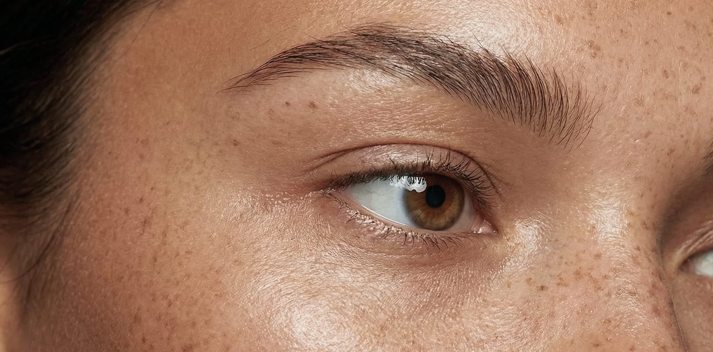Close-up of a person's eye with light brown iris and defined eyebrows.