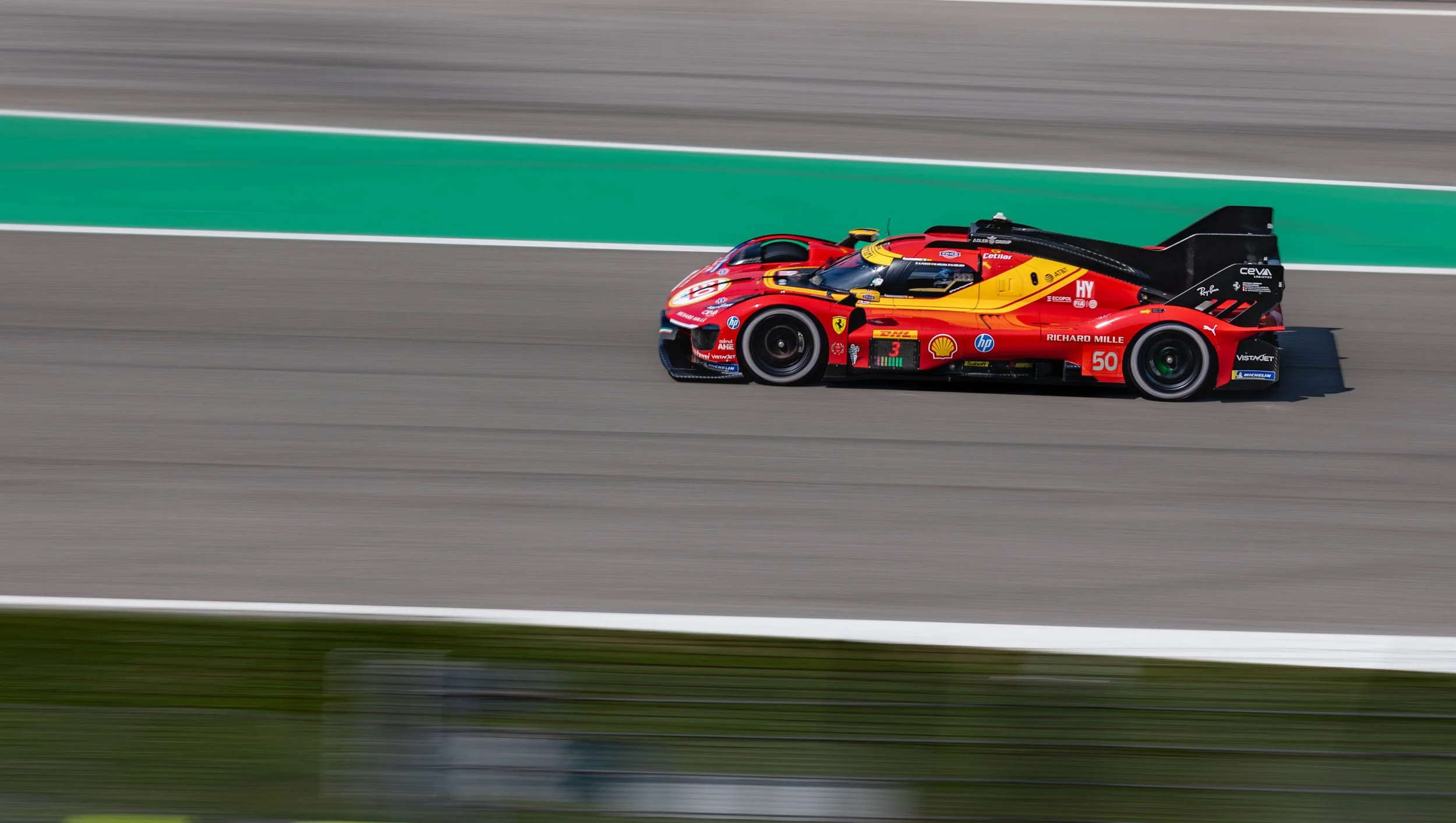 A red race car speeding on a racetrack with green and gray markings, in motion blur.
