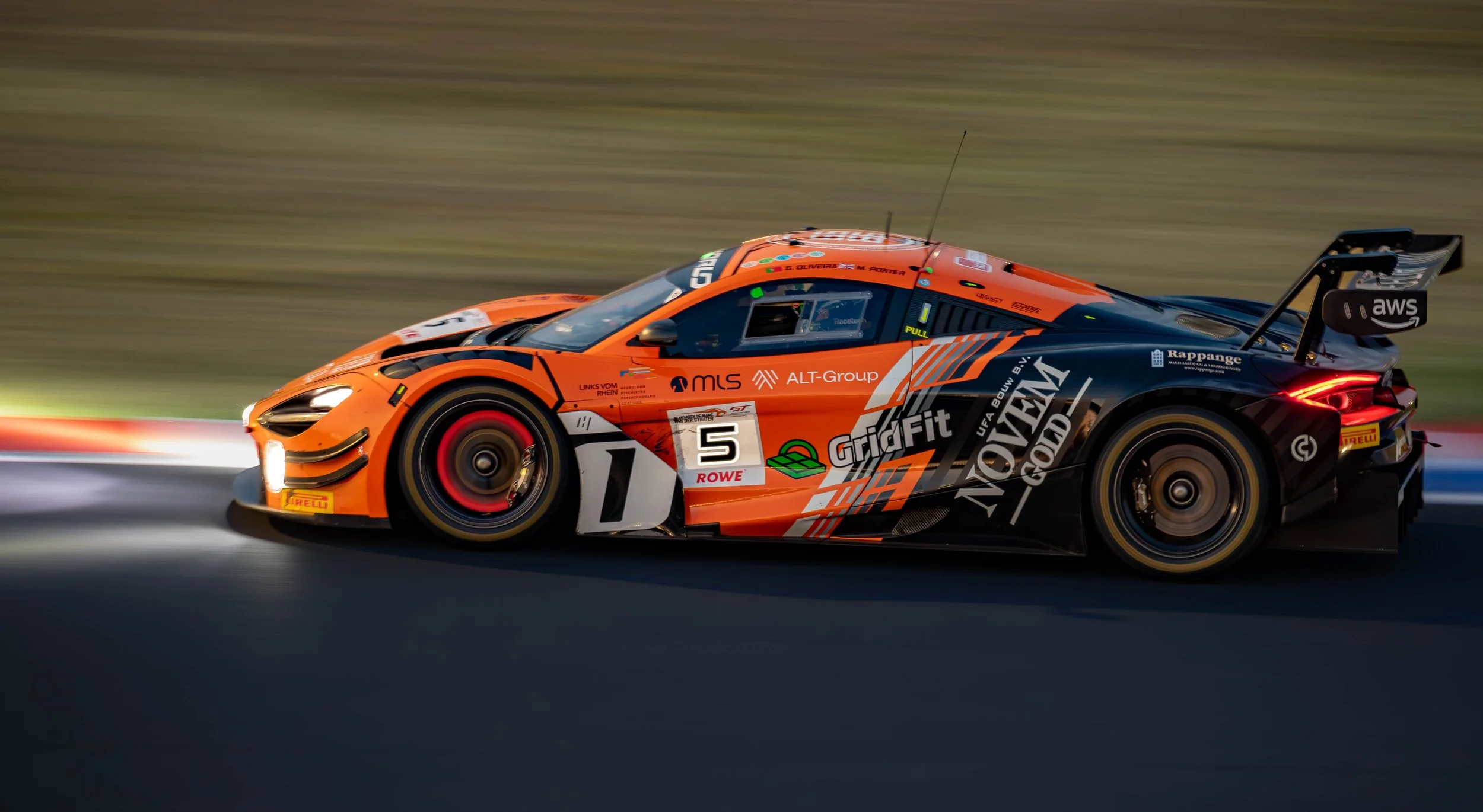 An orange and black racing car on a race track, in motion, with sponsorship logos and the number 5 on its side.