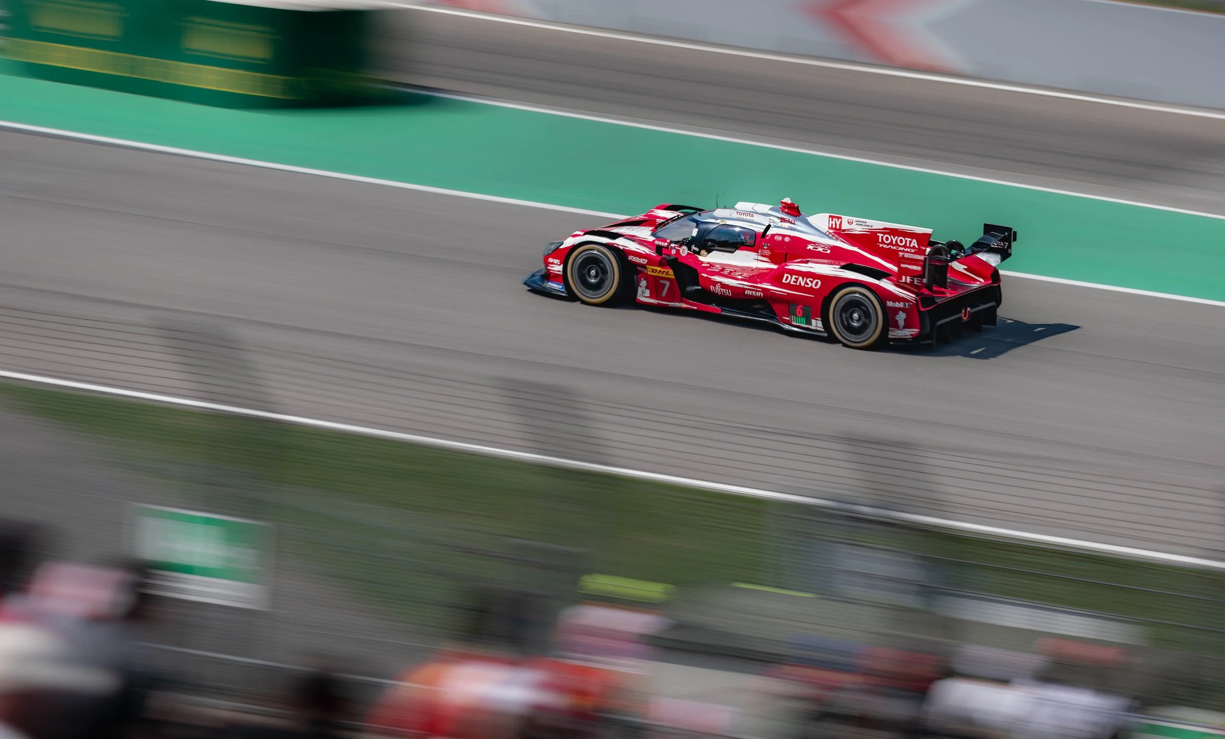 A red and white racing car speeding on a racetrack with blurred background.