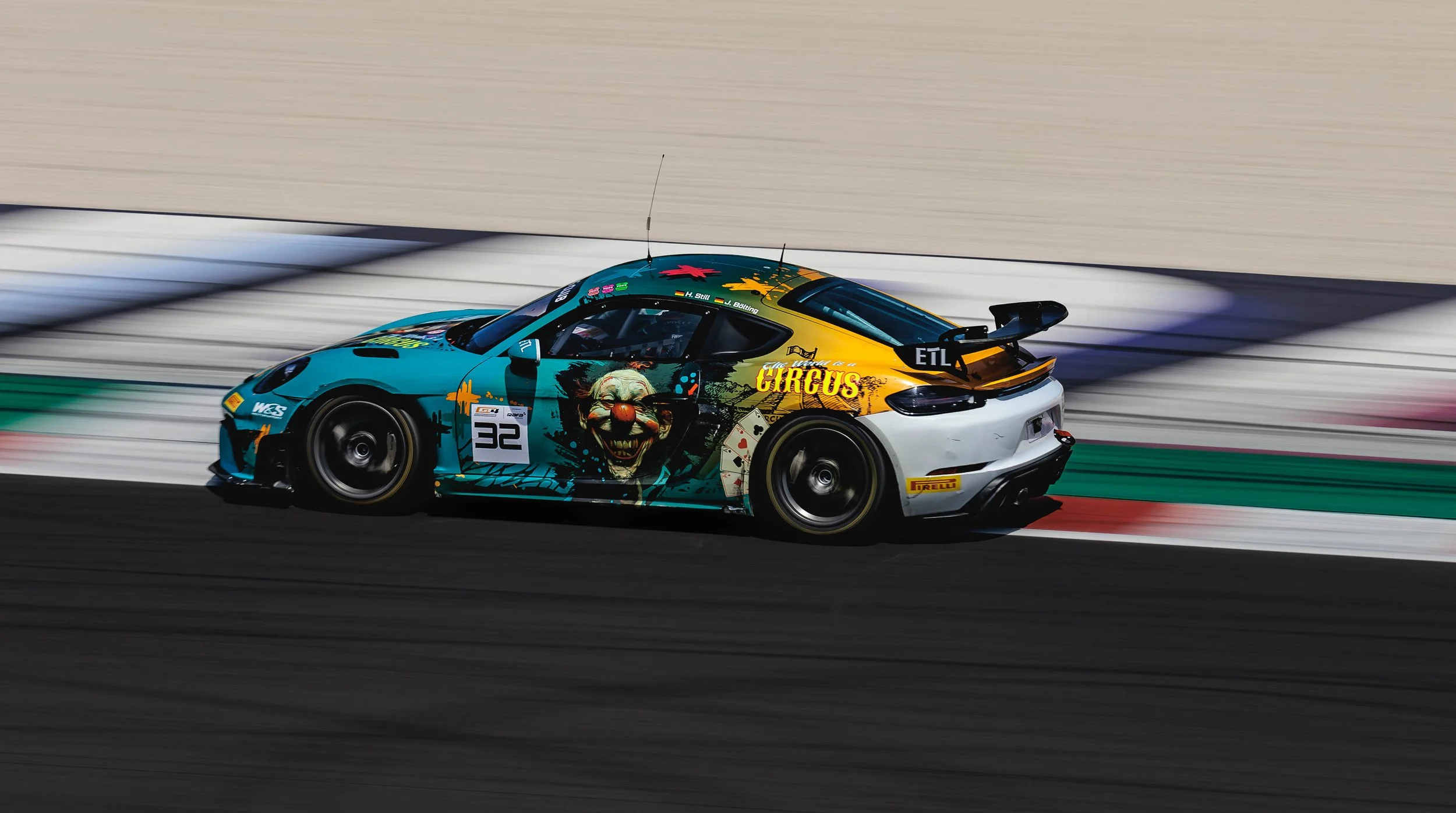 Race car with clown face graphic and circus themed artwork racing on track.