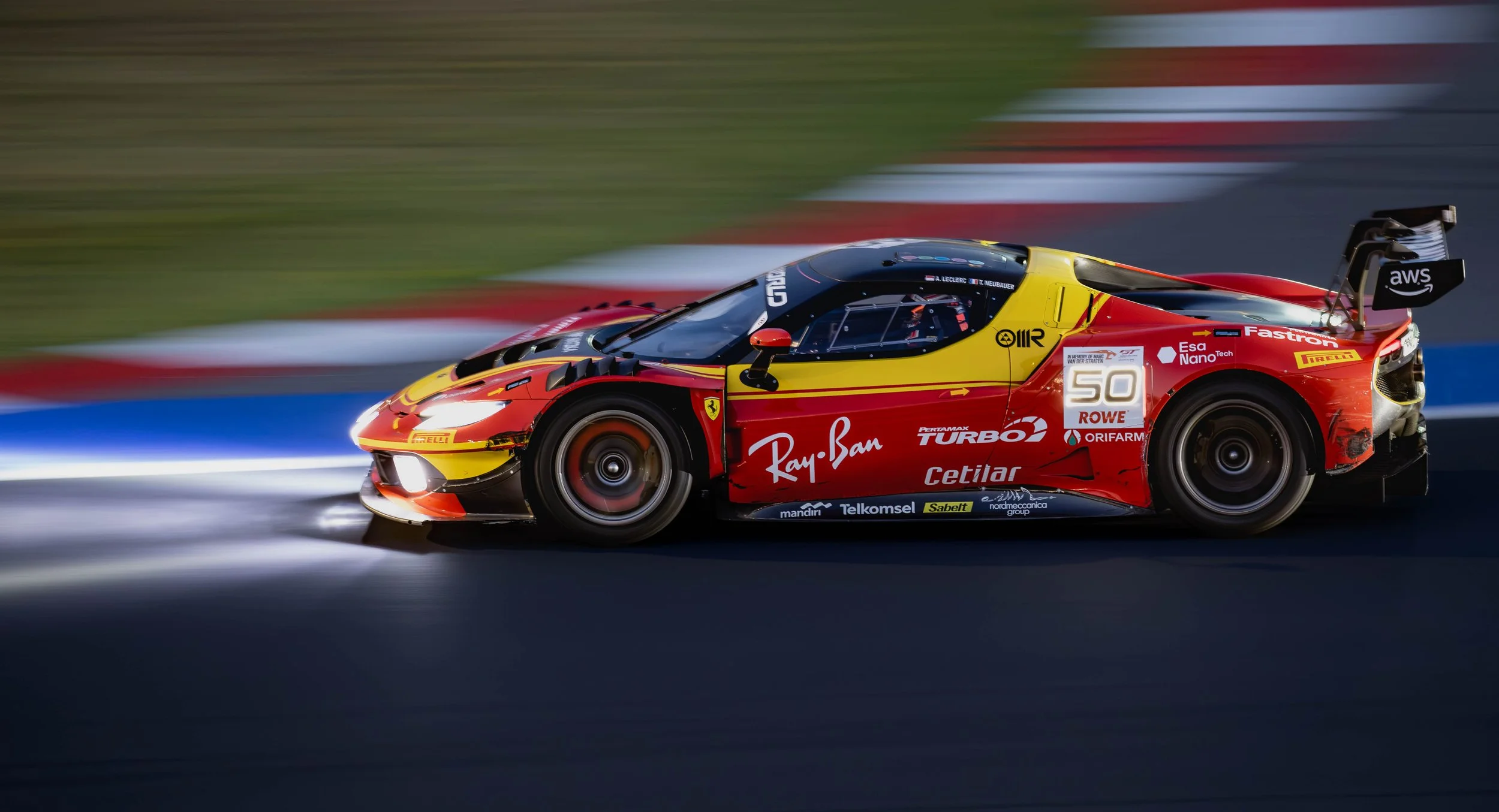 A red and yellow race car speeding on a track at night, with a blurred background.