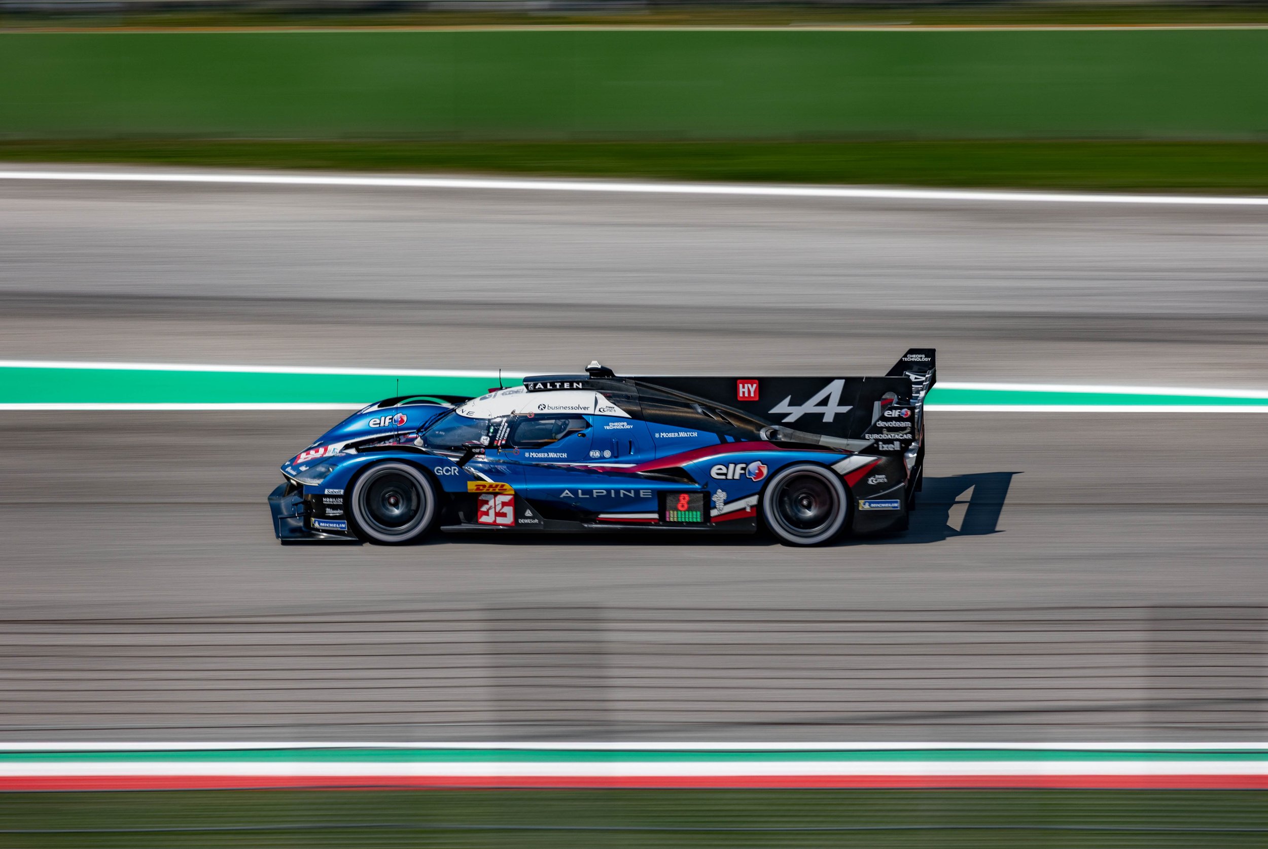 A blue and black race car with the number 35 on it driving on a racing track with blurred green and gray background.
