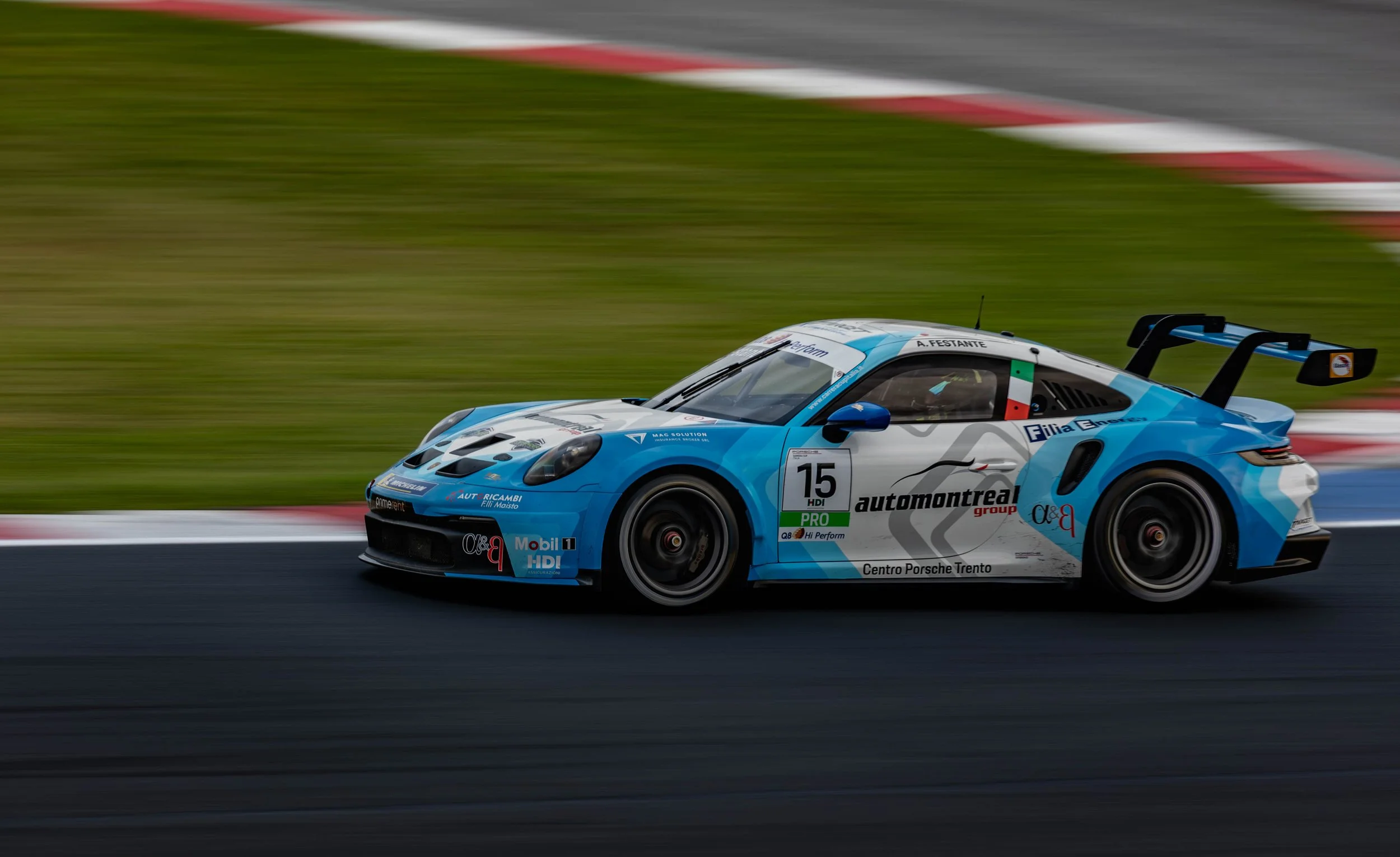 A blue and white race car speeding on a track with a blurred background of grass and pavement.