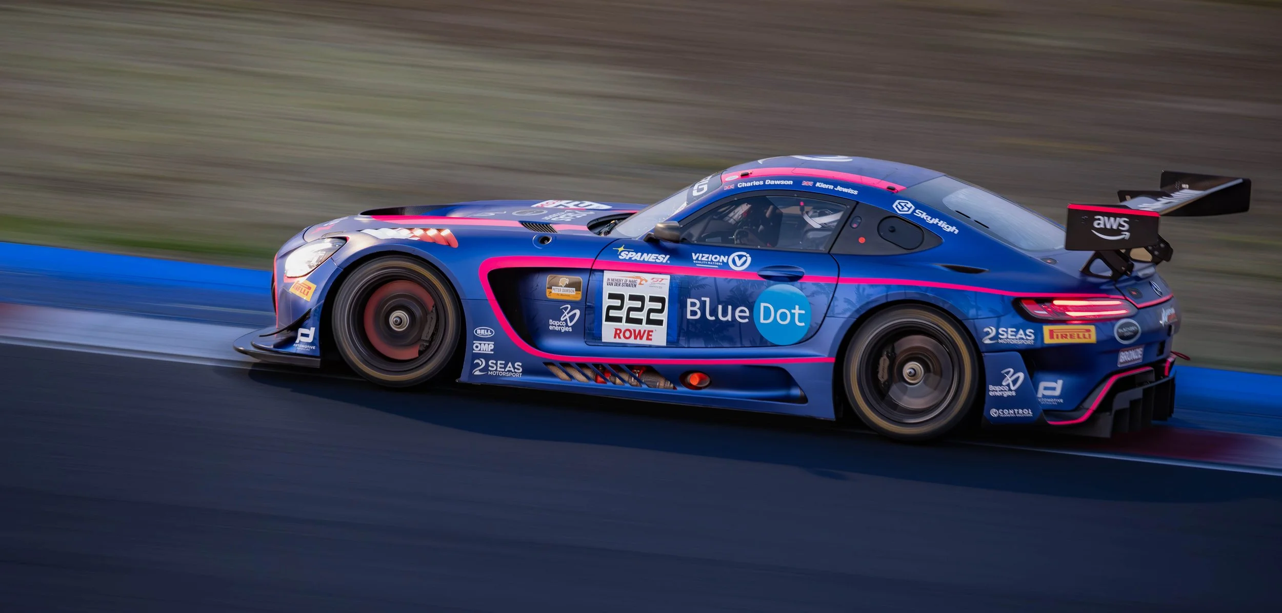 A blue race car with pink accents moving quickly on a race track.