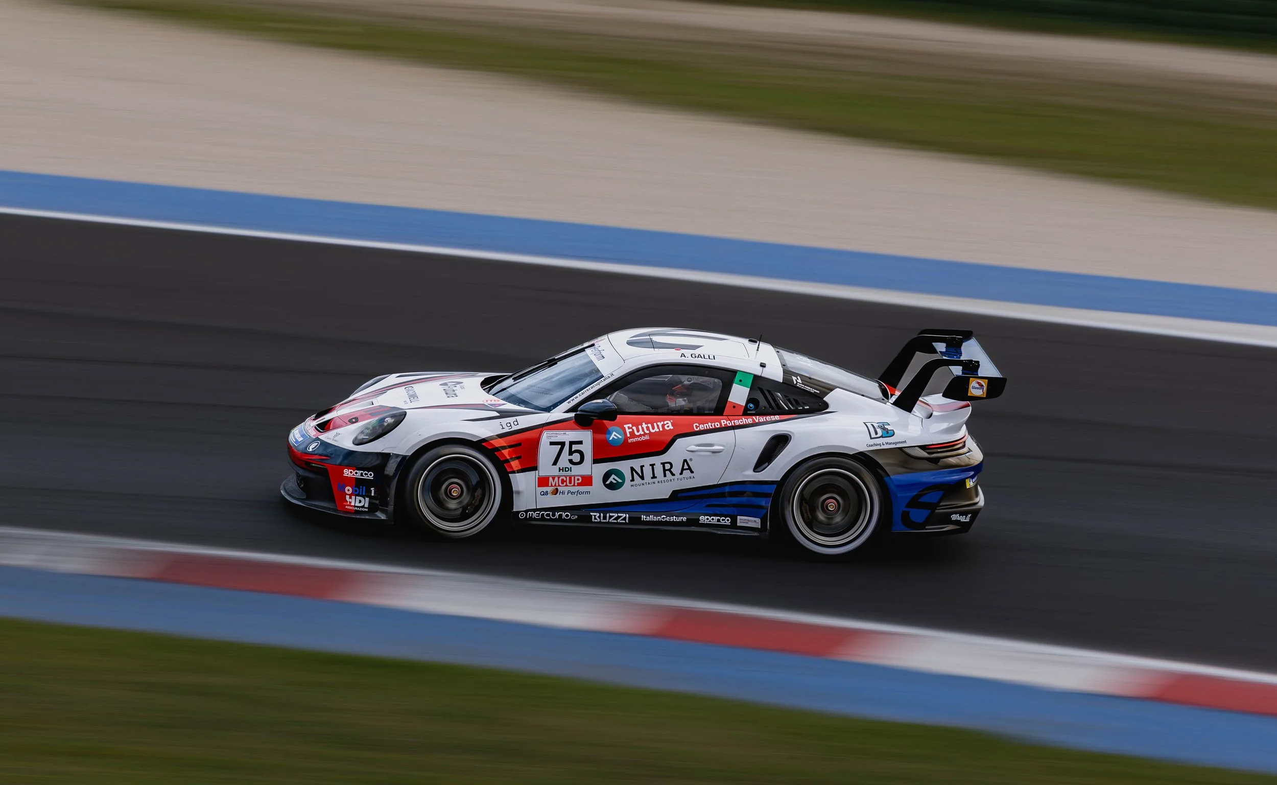 A race car speeding on a track with motion blur in the background. The car is predominantly white with red, blue, and black accents, featuring various sponsor logos and the number 75.