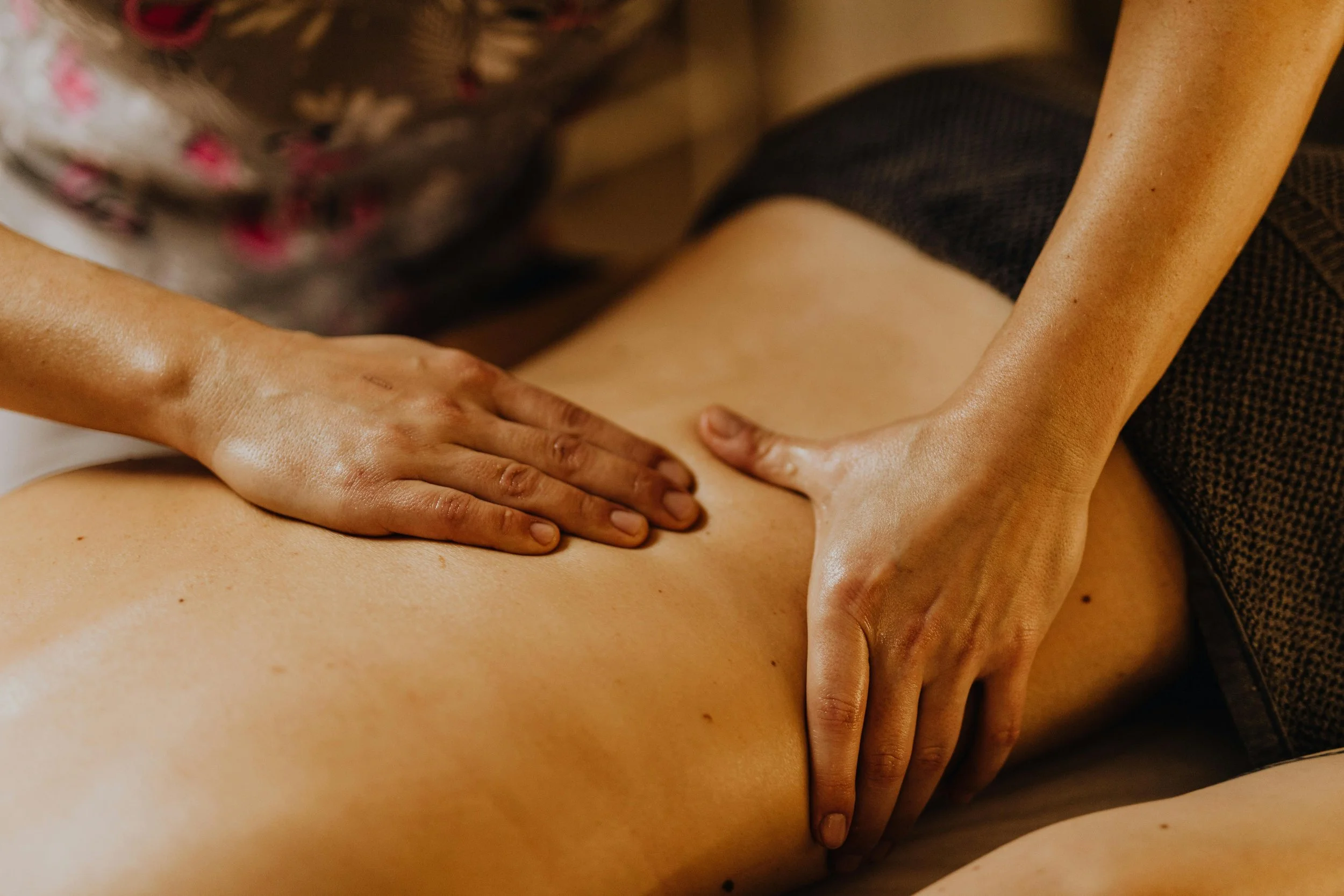 A massage therapist giving a massage to a person's back, with the person's back fully exposed and the therapist using both hands to apply pressure.