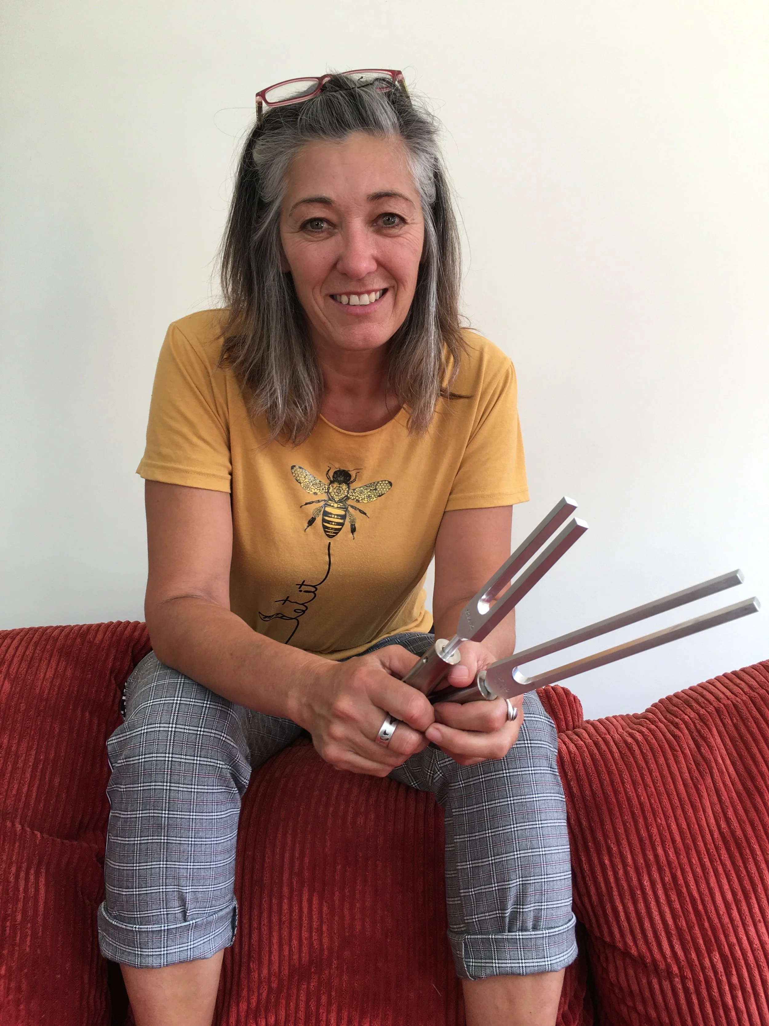 A woman with gray hair and glasses on her head, smiling, sitting on a red couch and holding a flaming torch.