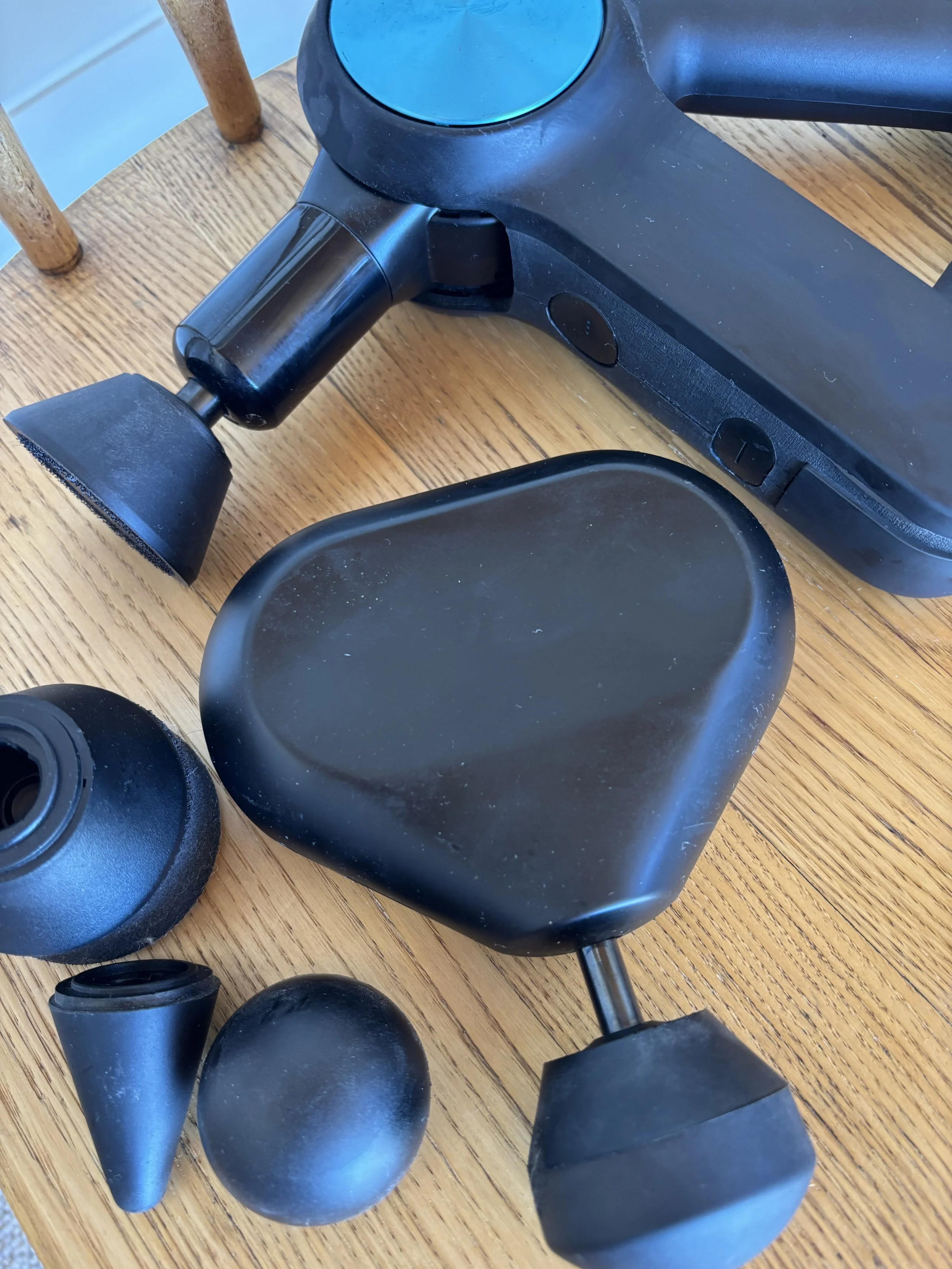 Disassembled black electronic massage device with various attachments on a wooden table.