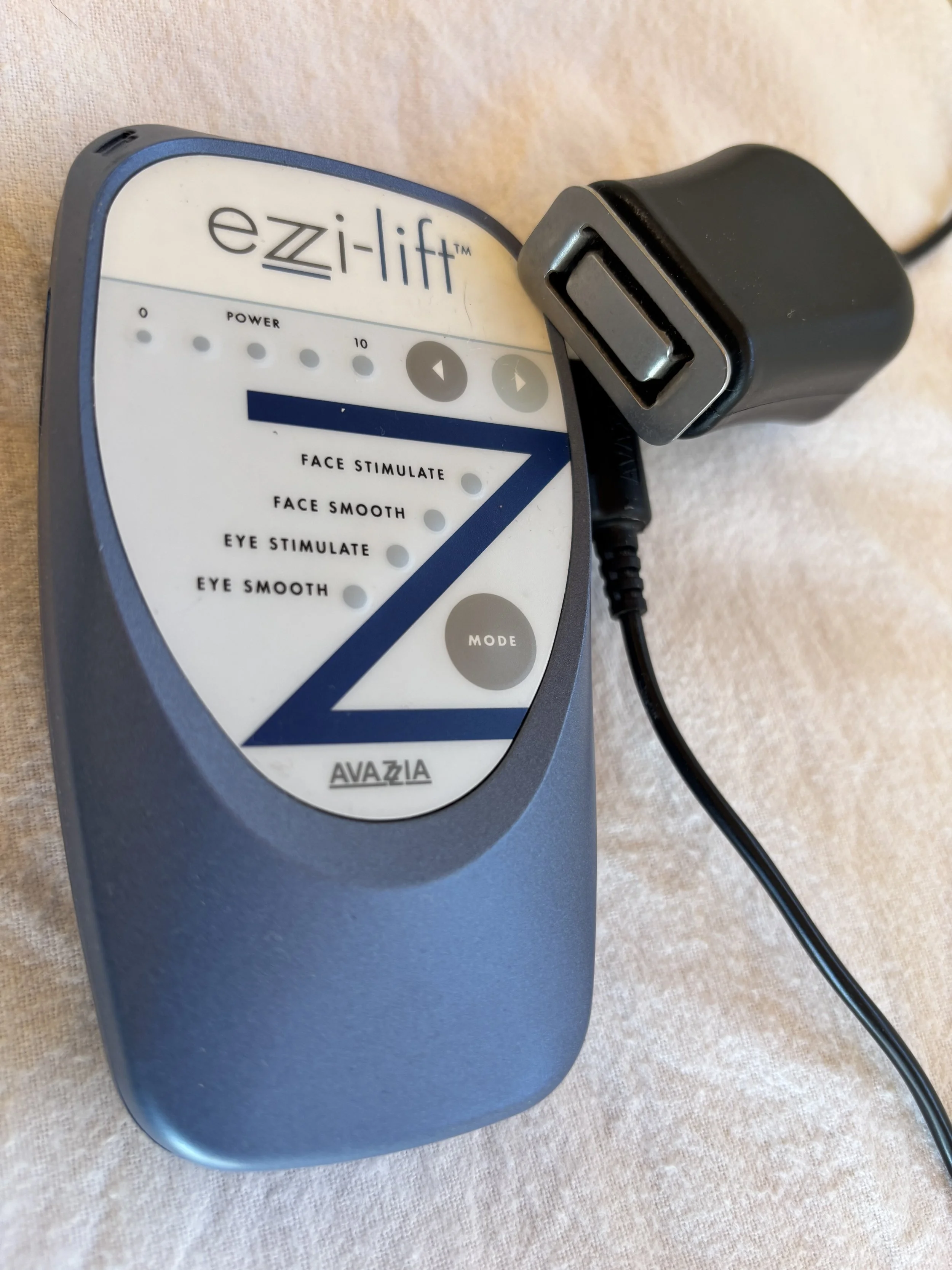 A handheld therapy device labeled 'ezi-lift' with buttons for power, mode, and adjustable levels, connected to a power adapter.