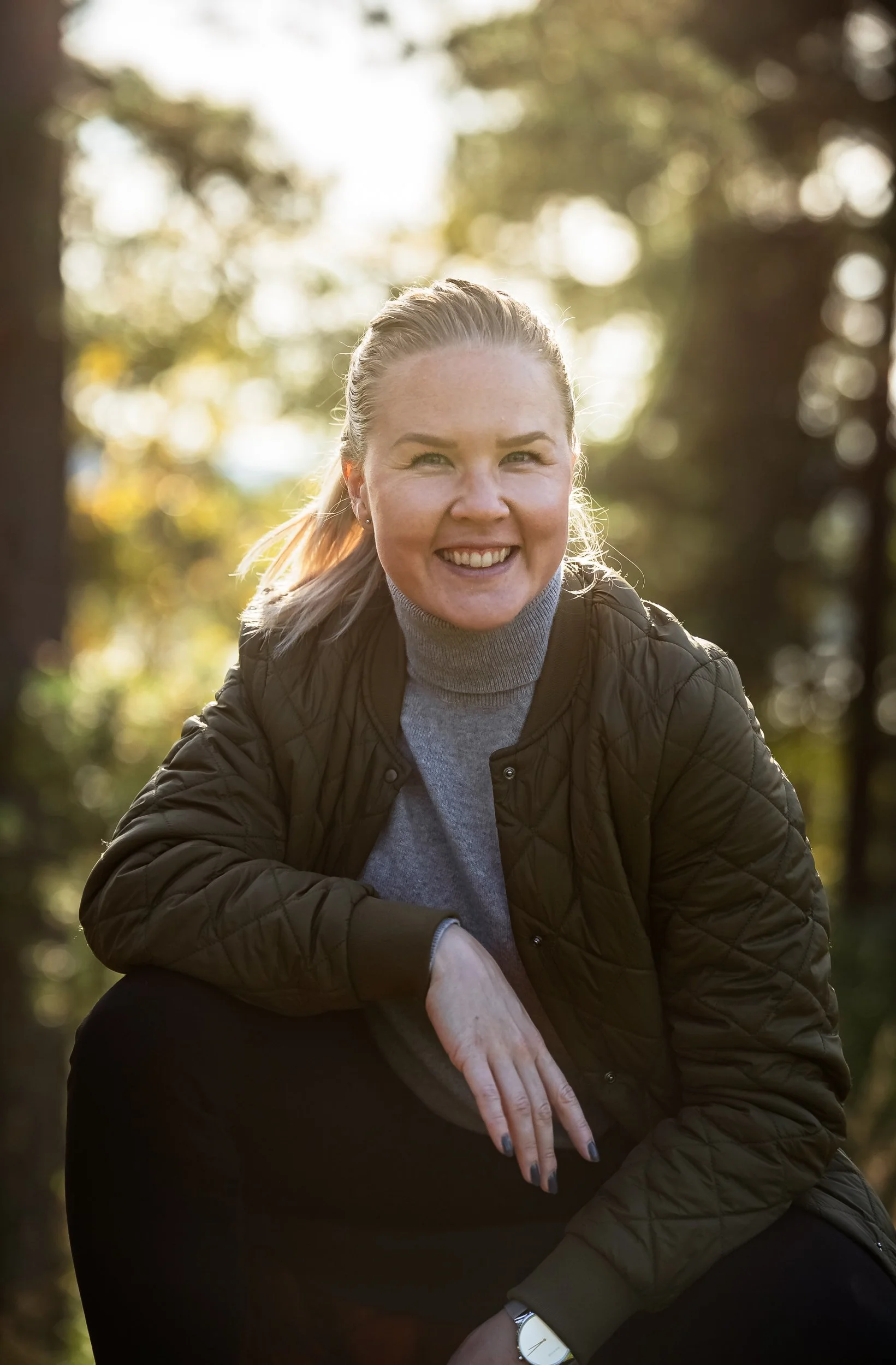 Suvi Nisula hymyilee ja katsoo kameraan syksyisessä metsässä. Suvilla on yllään harmaa neule ja vihreä tikkitakki, ja hän näyttää hyvävoimaiselta.