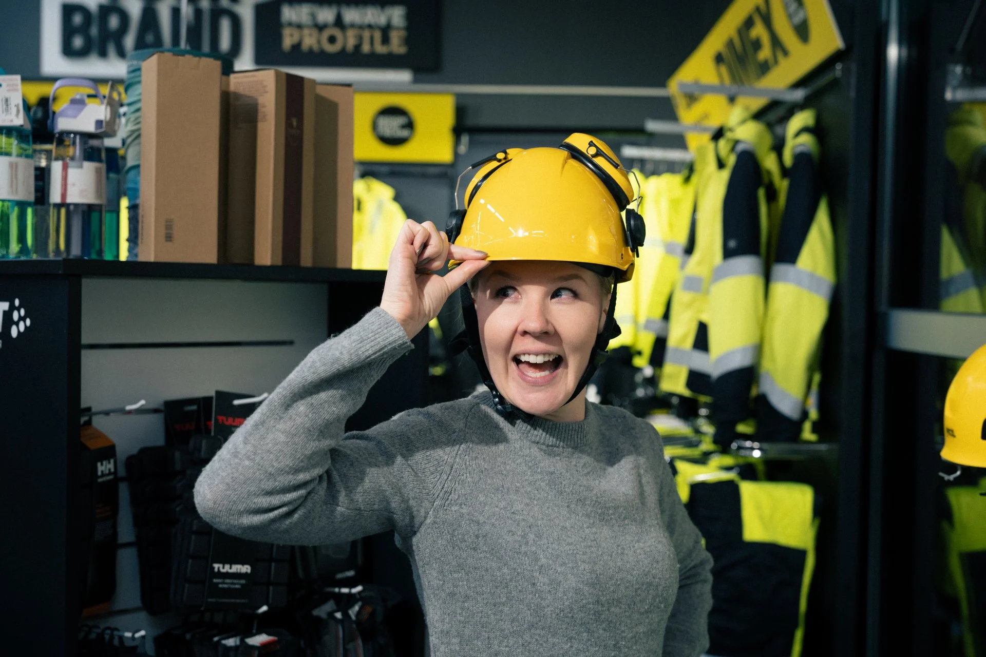 Suvi Nisula Suomen Brodeerauksen työ-, edustus- ja liikelahjamyymälässä työvarustemallina, työmaakypärä päässä iloisesti hymyillen.