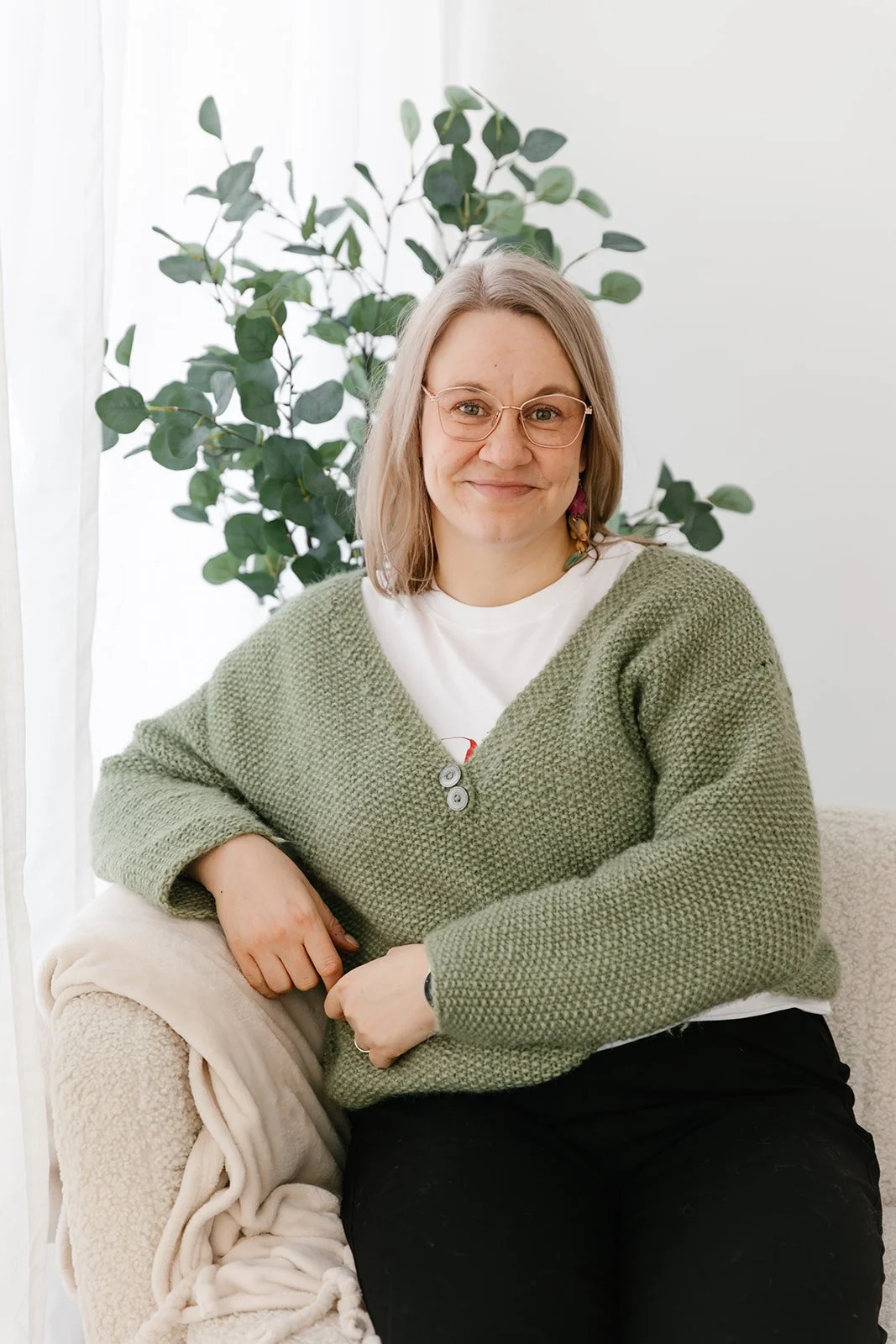 Lempeä Terapiapalvelut terapeutti istuu sohvalla ja katsoo kameraan hymyillen.