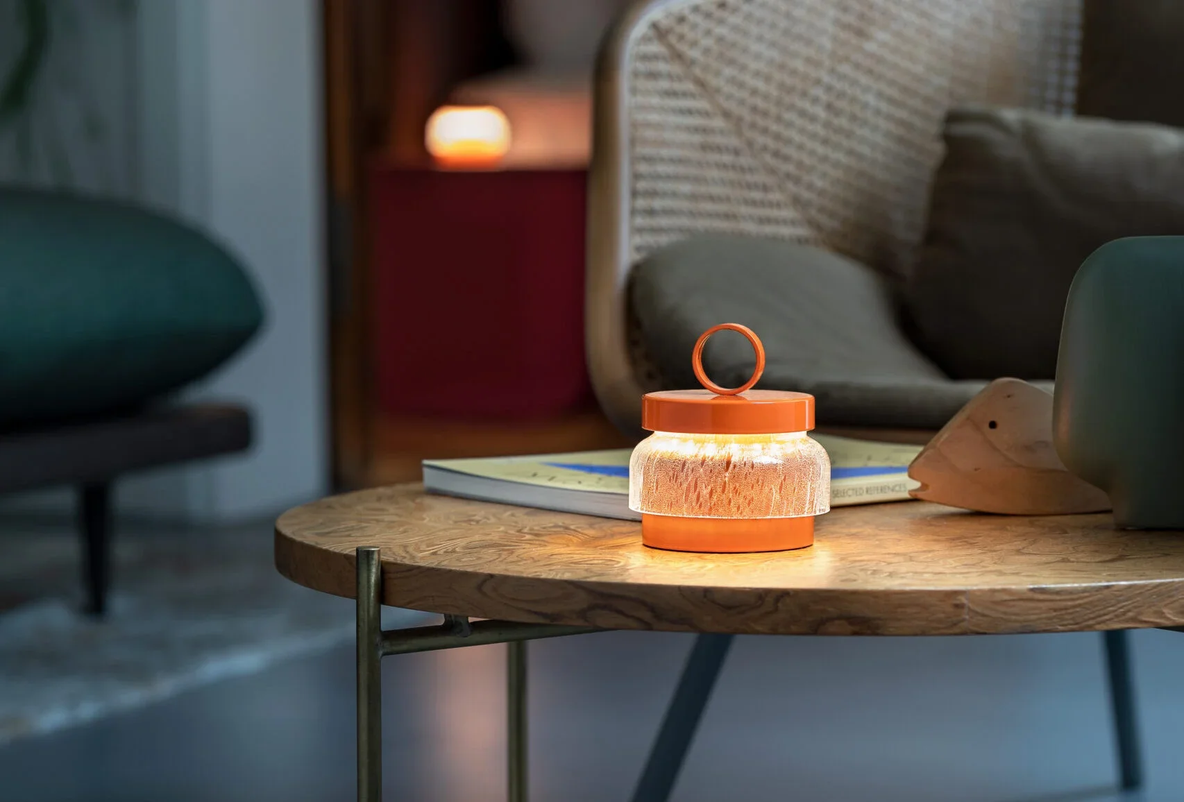 A wooden table with a lantern-shaped lamp, a book, and a wooden object, with a sofa and a side table with a lamp in the background.