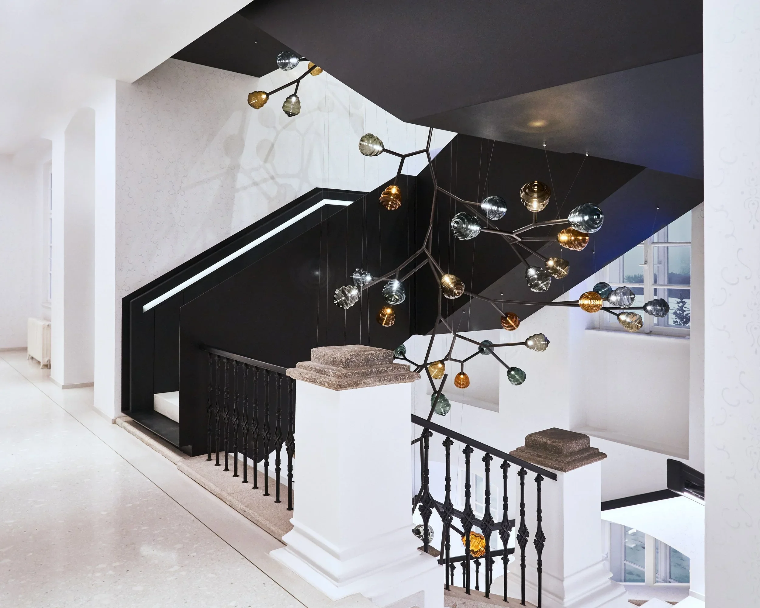 Modern staircase indoors with a black and white color scheme, contemporary chandelier with multiple glass orbs, and large windows with a view outside.