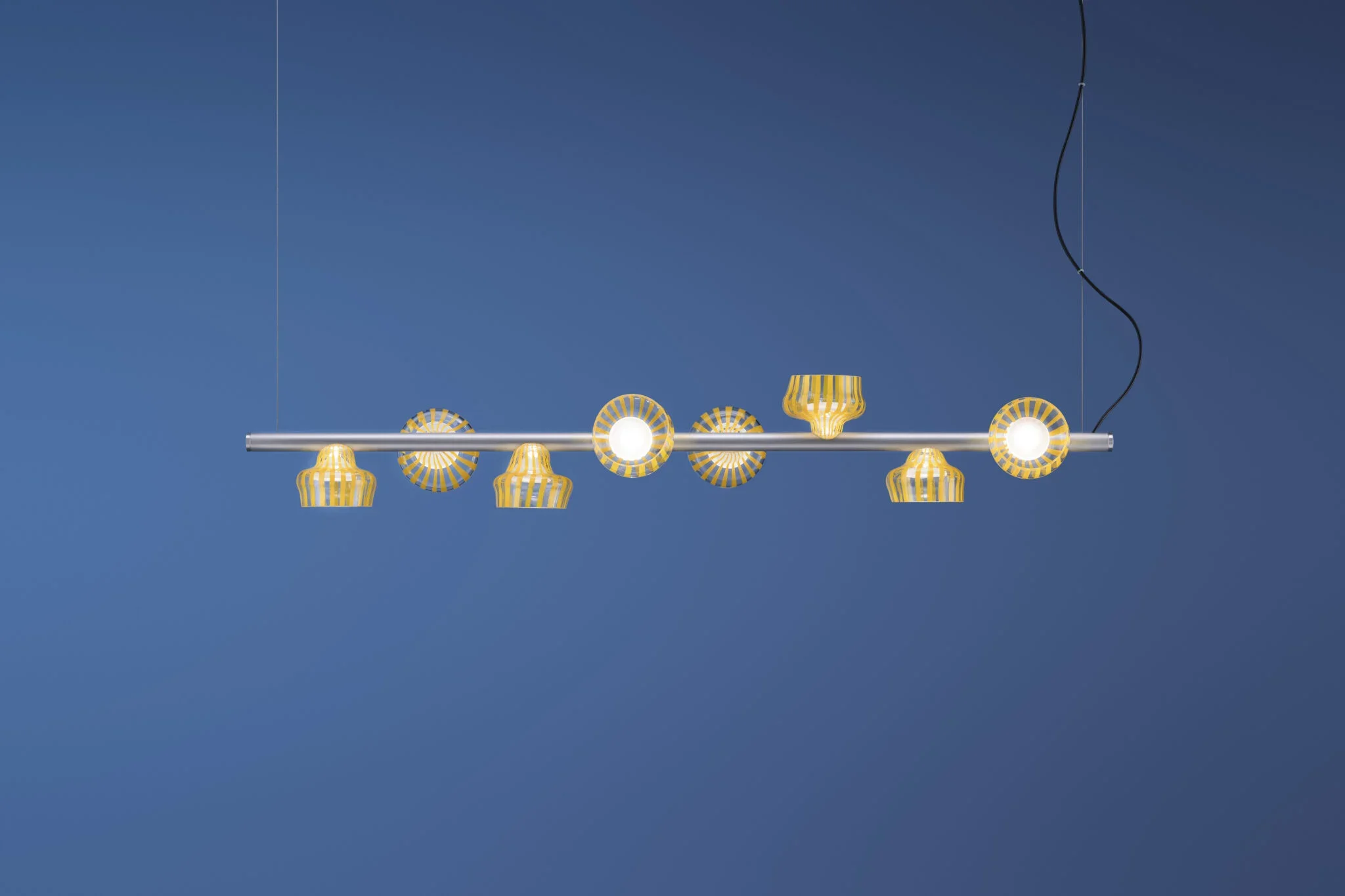 Modern chandelier with alternating yellow and white striped shades hanging from a blue ceiling.