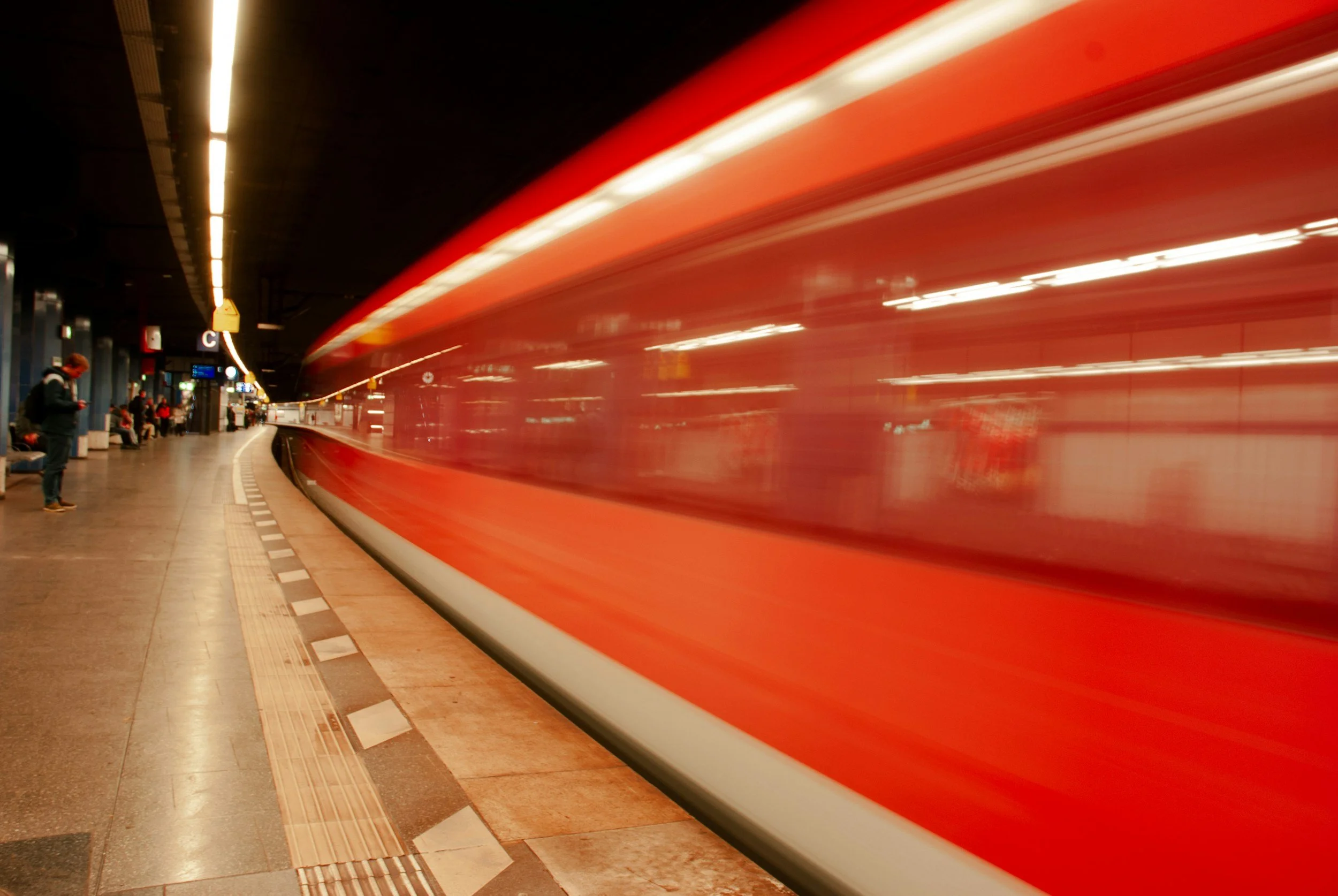 A train moving quickly through an underground station, with passengers waiting on the platform.