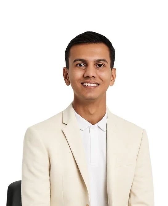 A young man with short black hair, smiling, wearing a white blazer and white shirt, sitting against a plain white background.