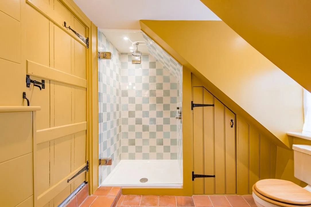 Bathroom with a walk-in shower featuring checkered tiles, yellow wooden panel walls, a toilet with a wooden seat, and brick-patterned floor tiles.