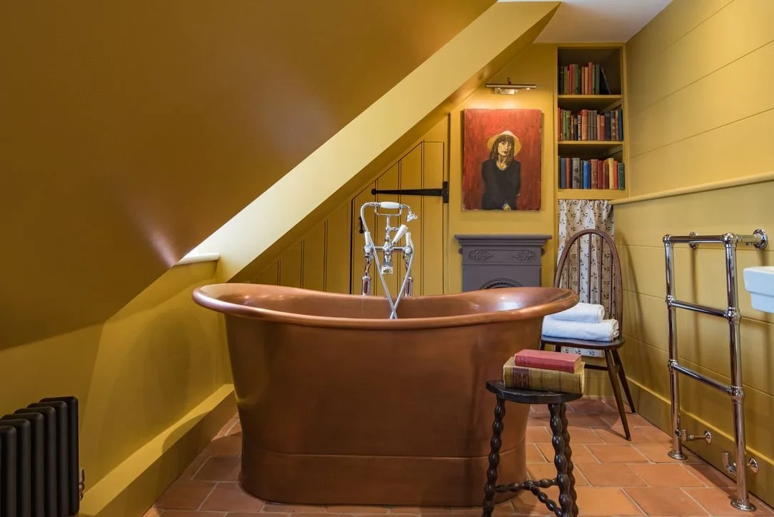 Vintage copper bathtub in a cozy attic bathroom with books and artwork.