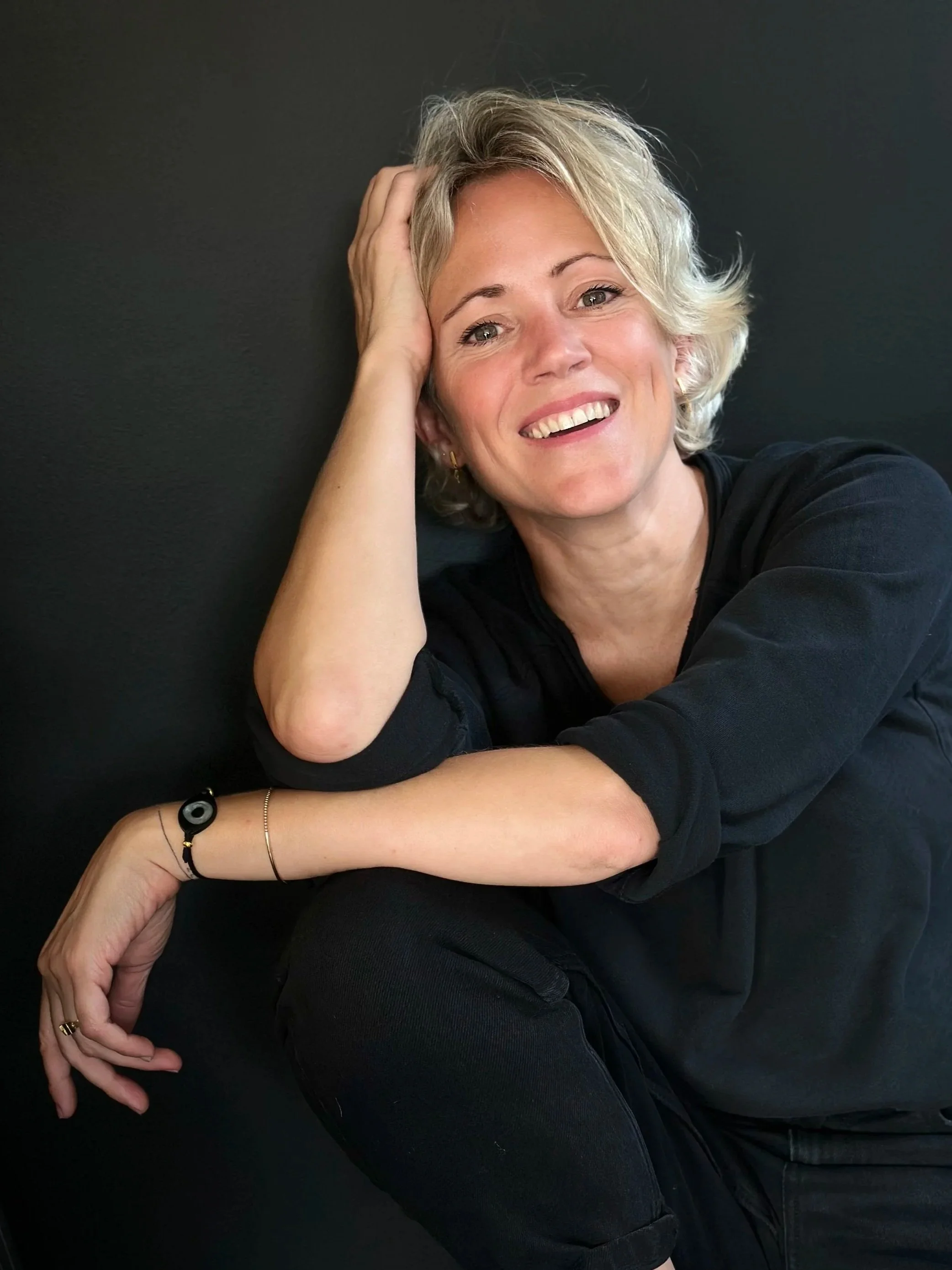 Portret van Florien, oprichtster van Ayurflo, zittend tegen een donkere achtergrond met een warme glimlach.