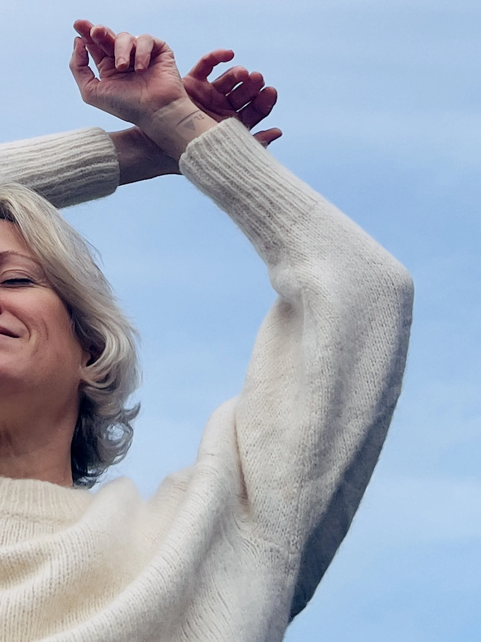 Vrouw met opgeheven armen tegen een blauwe lucht, symbool voor vrijheid en ontspanning.
